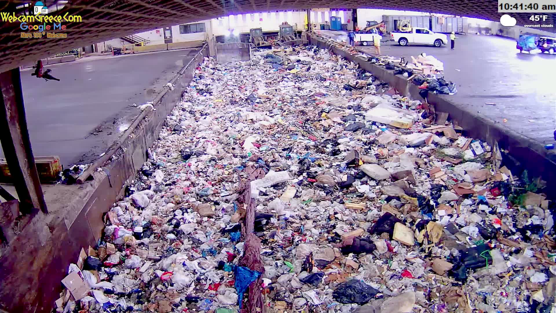 A large amount of trash is piled high in an outdoor receptacle under overcast skies.