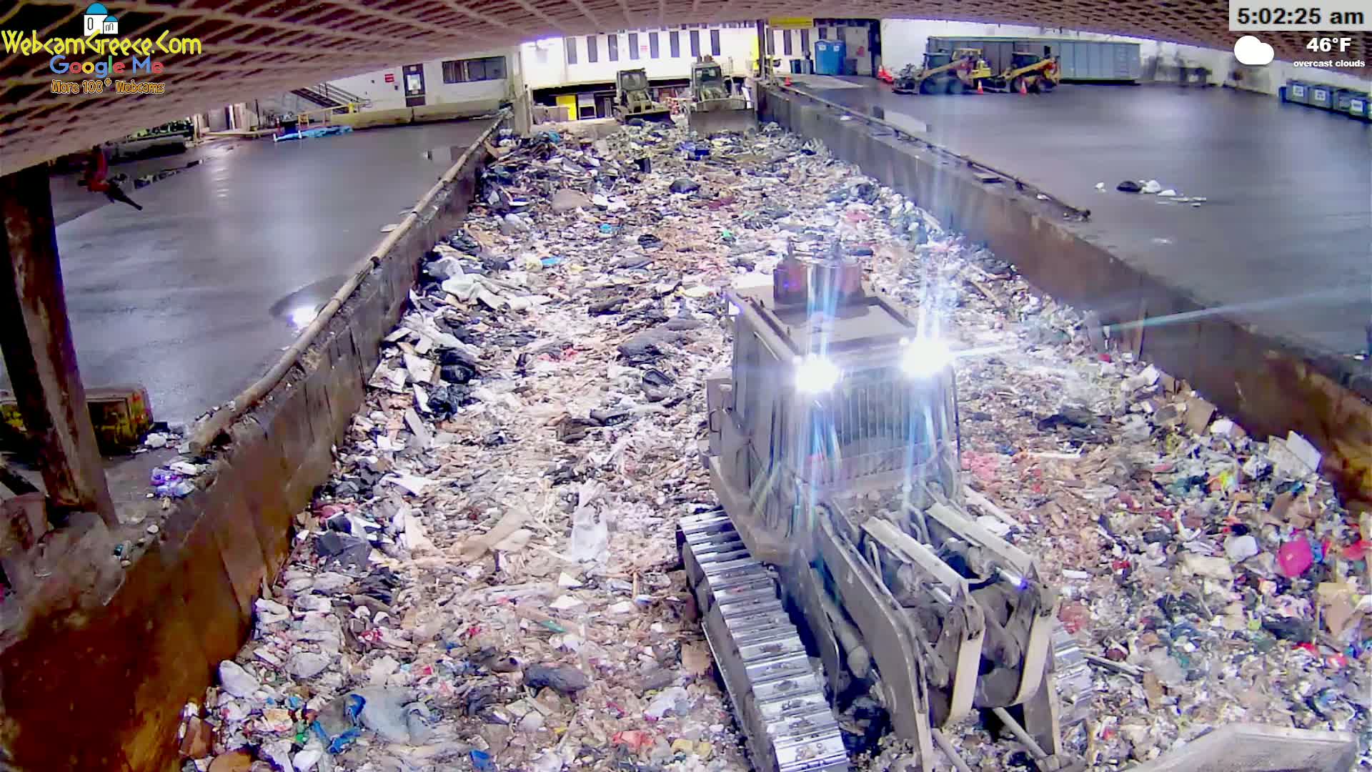 A bulldozer is working in a large, enclosed area filled with mounds of trash under overcast skies.