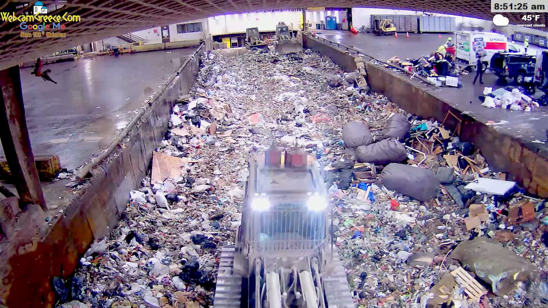 A bulldozer is working within a large, overflowing landfill under overcast skies at 45°F.