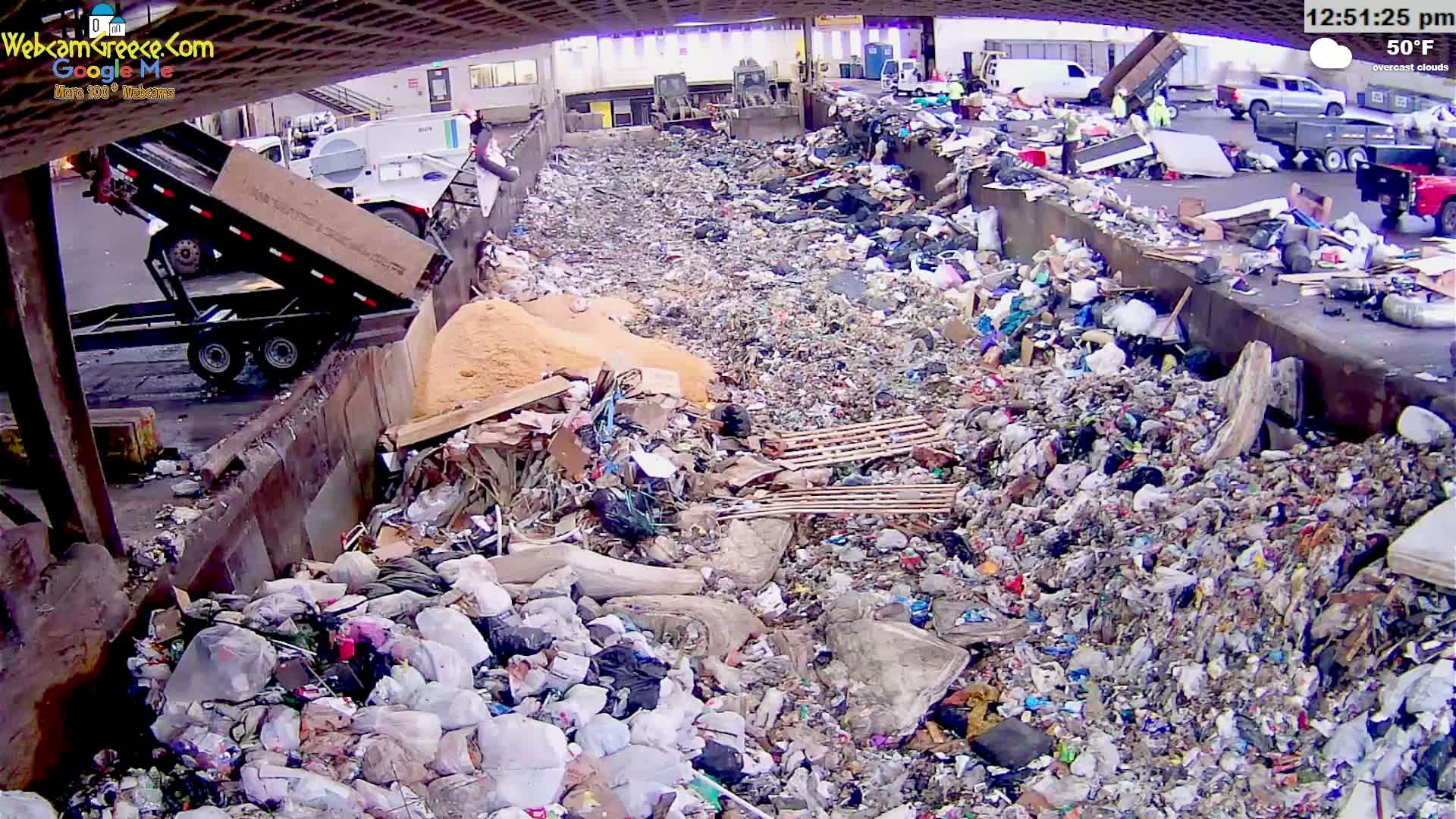 A large pile of garbage is being dumped from a truck into a landfill under overcast skies.