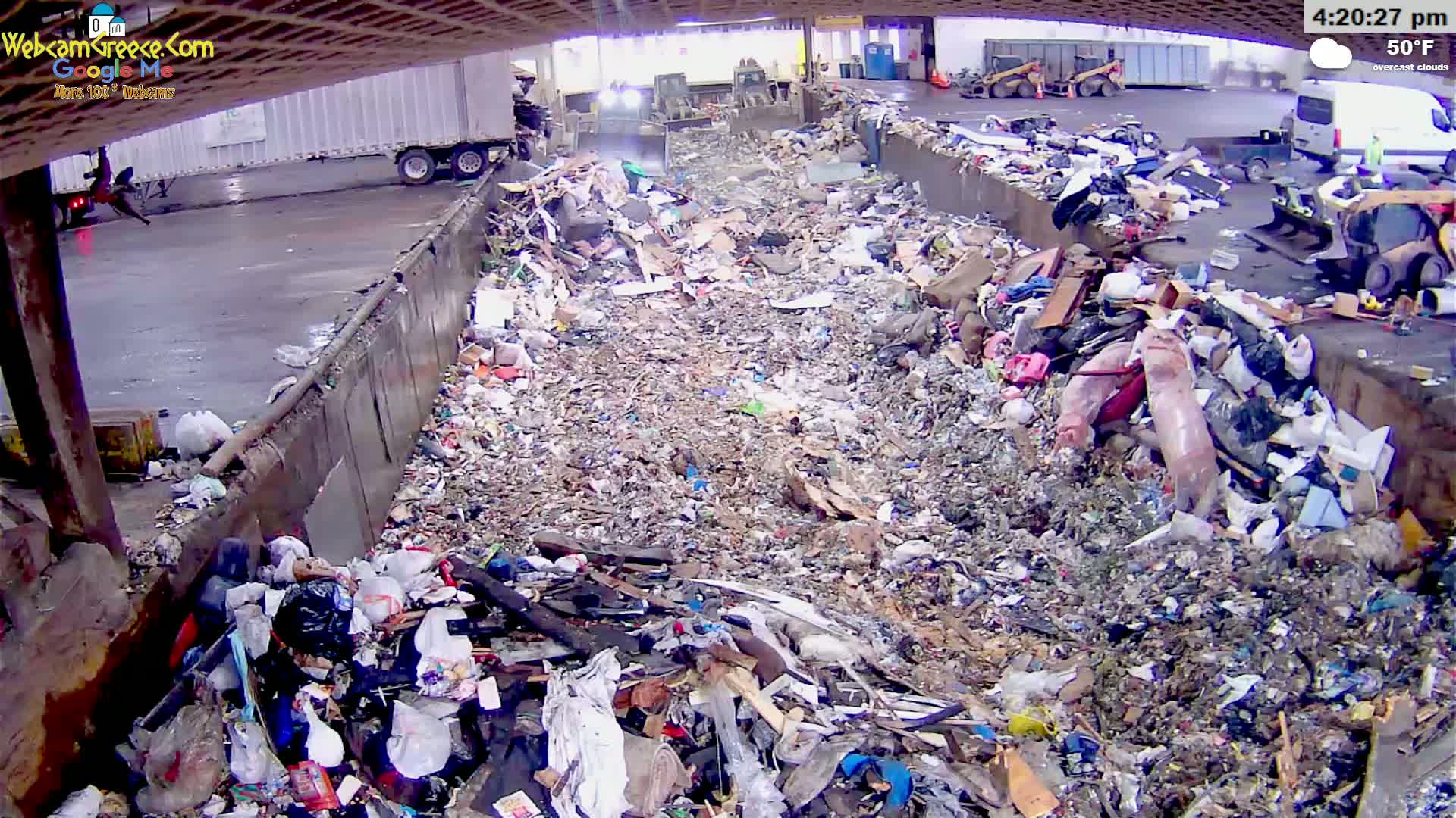 A large pile of trash is seen under overcast skies at 50°F, with industrial machinery and vehicles visible in the background.