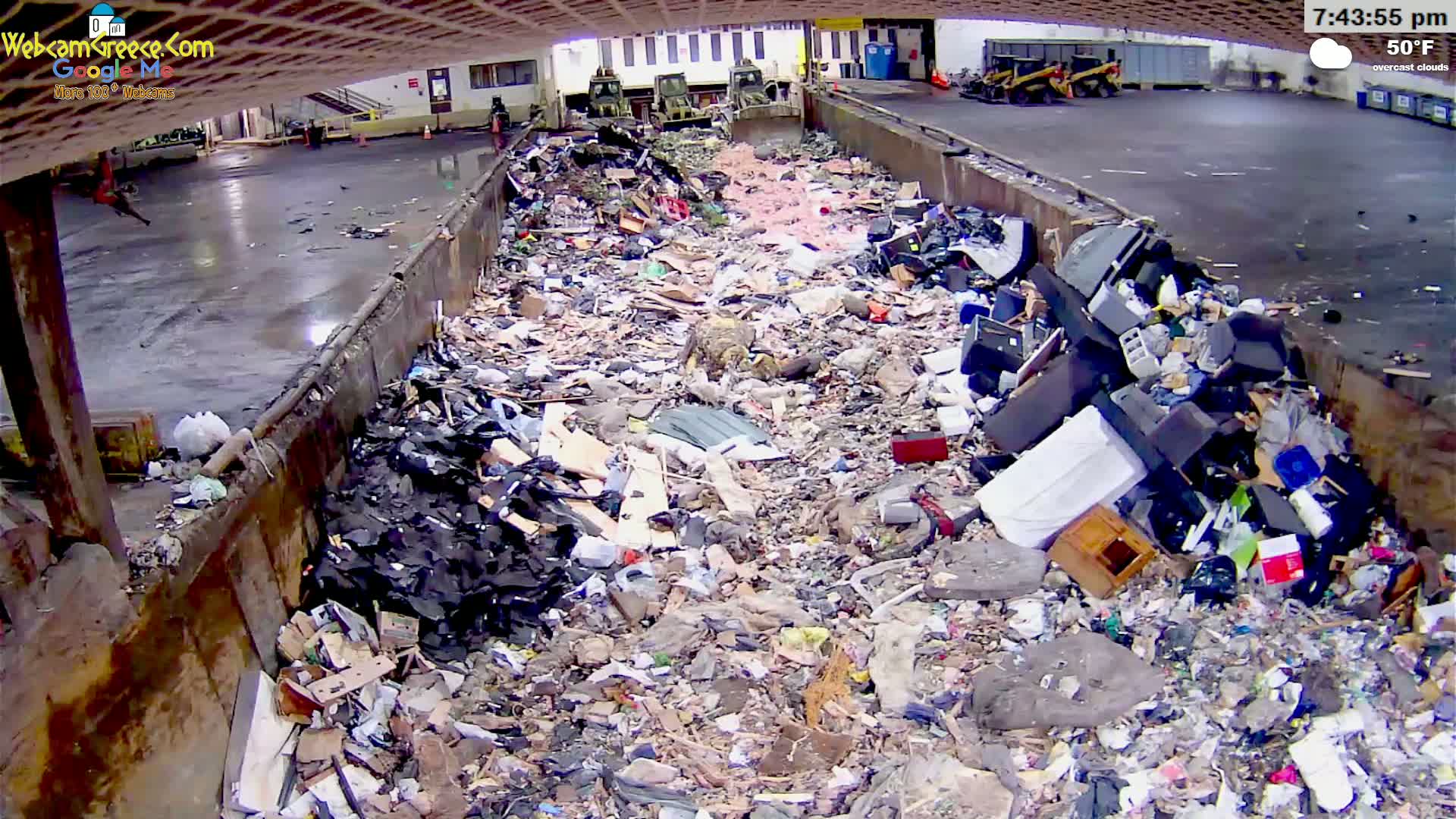 A large pile of mixed waste sits in an open-air refuse container under overcast skies.