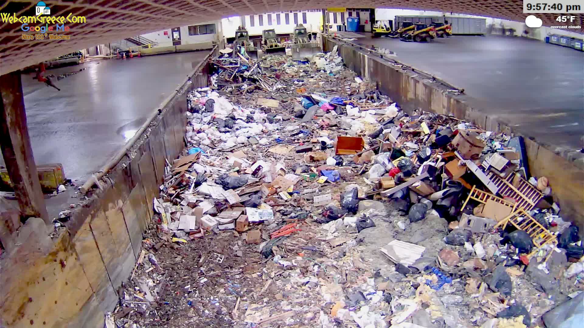 A large pile of trash and debris fills a concrete trough under overcast skies, with the temperature at 45°F.