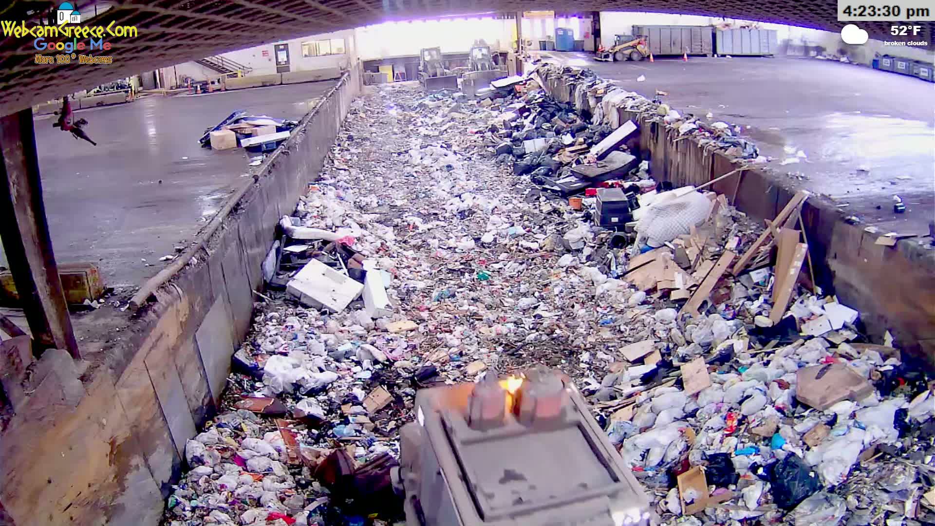 A large pile of trash and debris fills a long, narrow trench outdoors under broken clouds on a 52°F day.