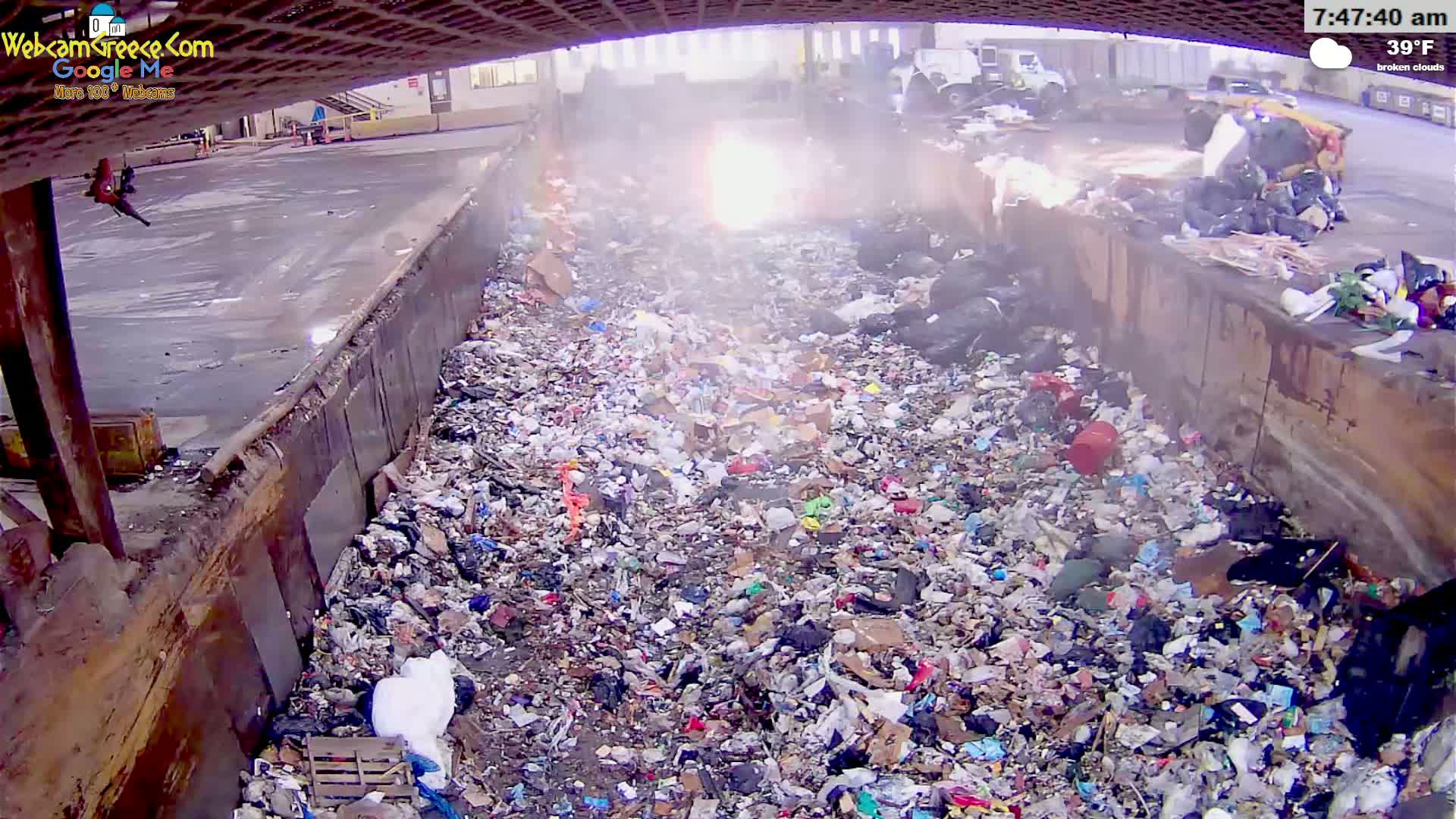 A large pile of garbage is seen in a waste disposal area under broken clouds, with a temperature of 39°F.