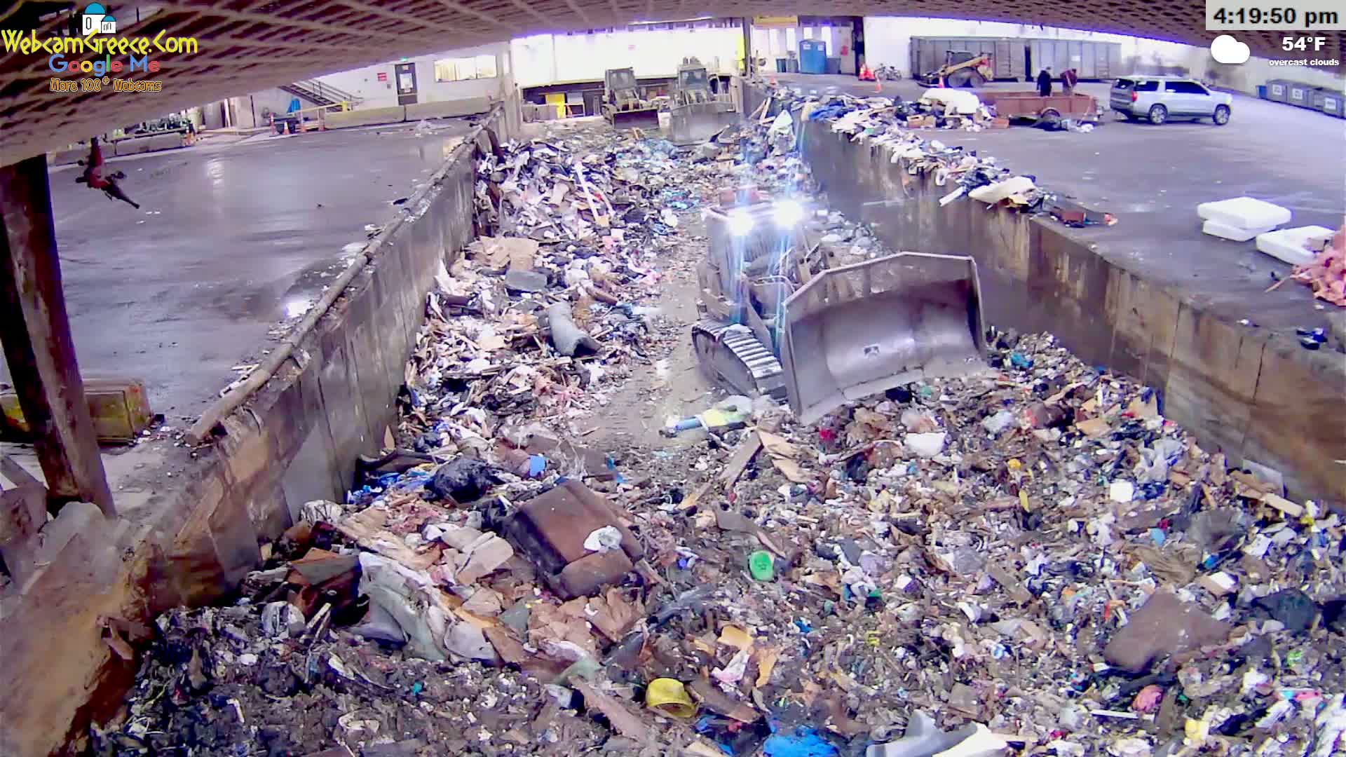 A bulldozer is working in a large pit filled with a substantial amount of garbage under overcast skies.
