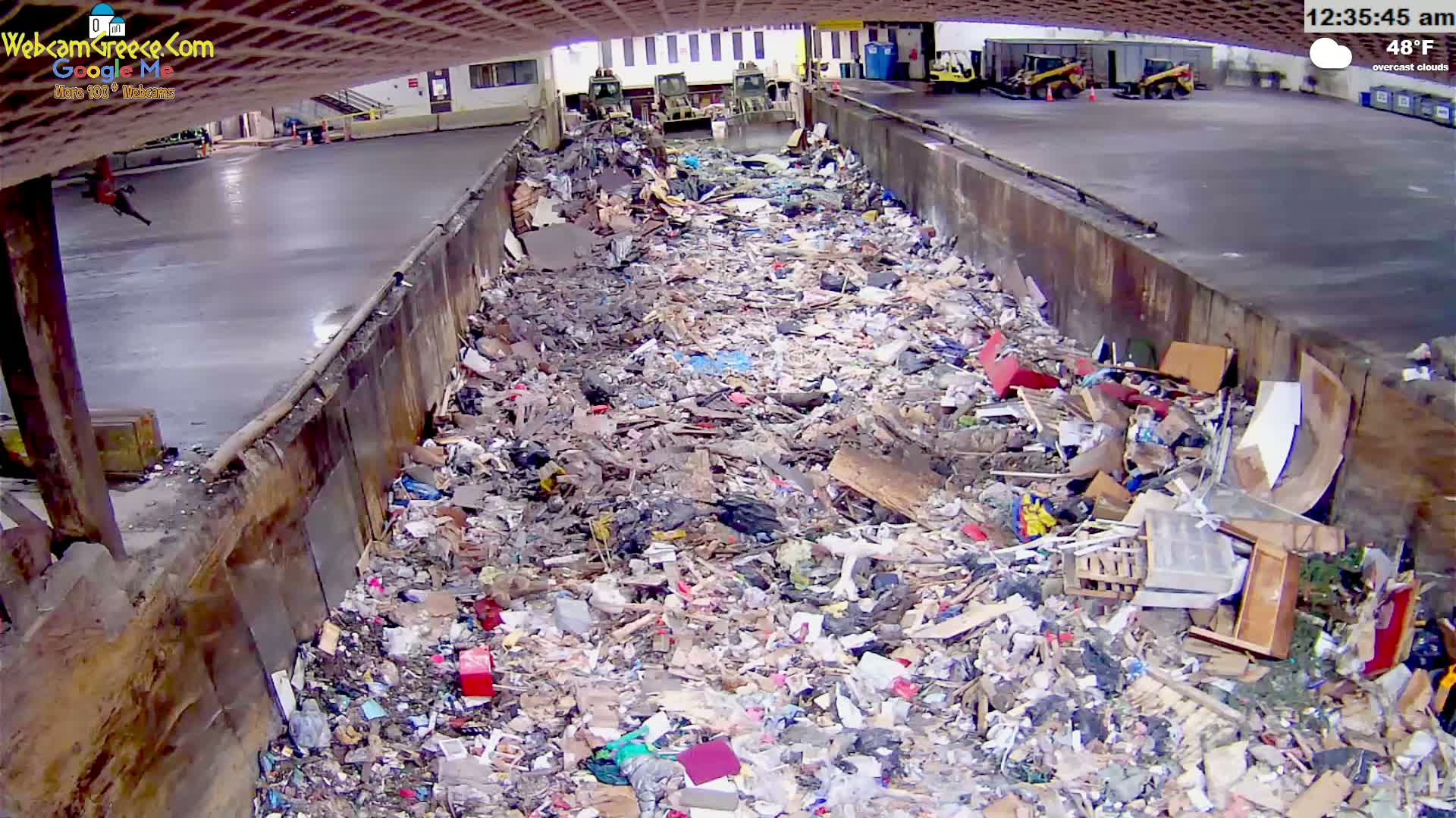 A large pile of trash is filling a concrete-walled receptacle under an overcast sky at 48°F.