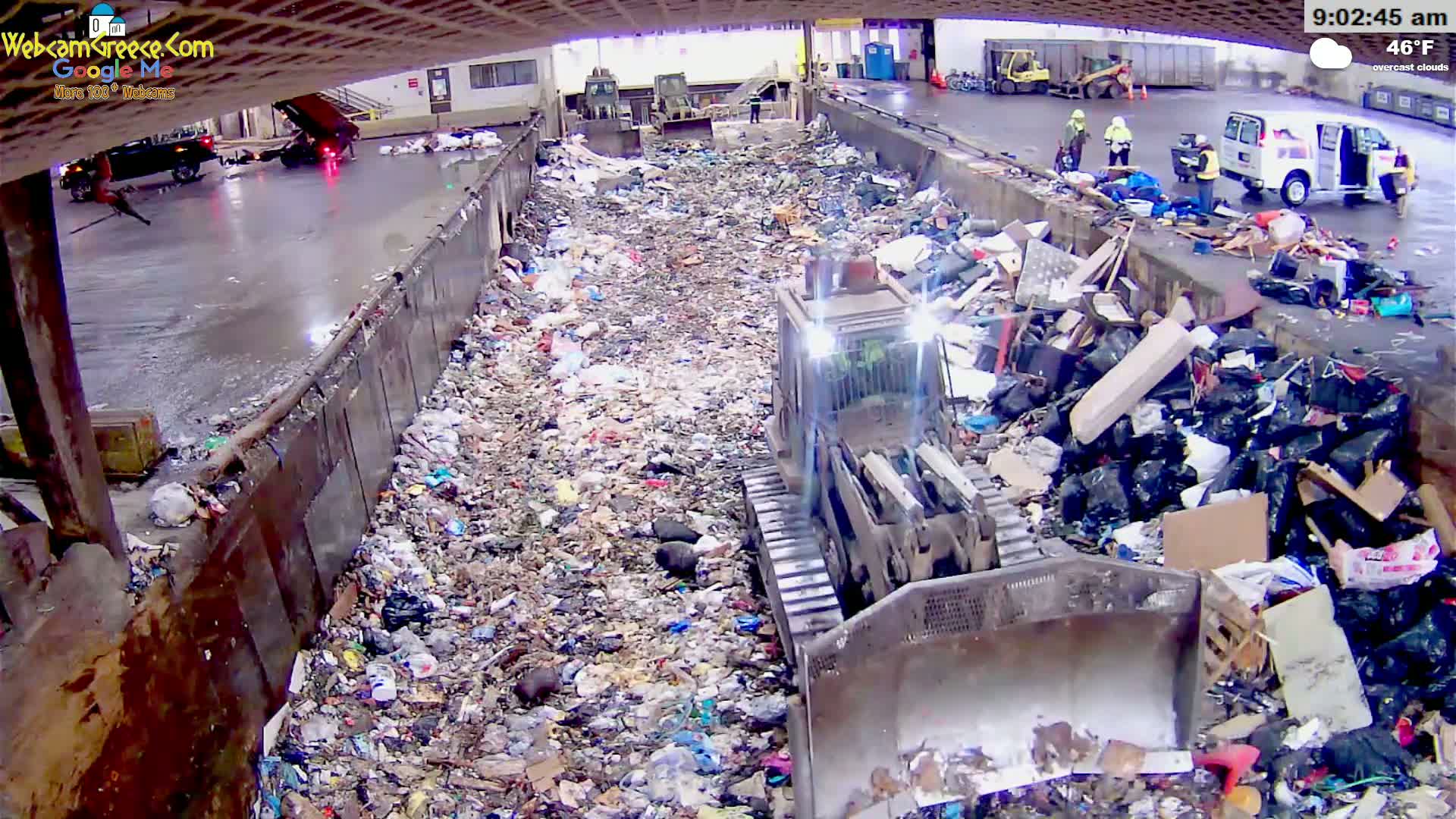 A bulldozer is working in a large, overflowing landfill under overcast skies.
