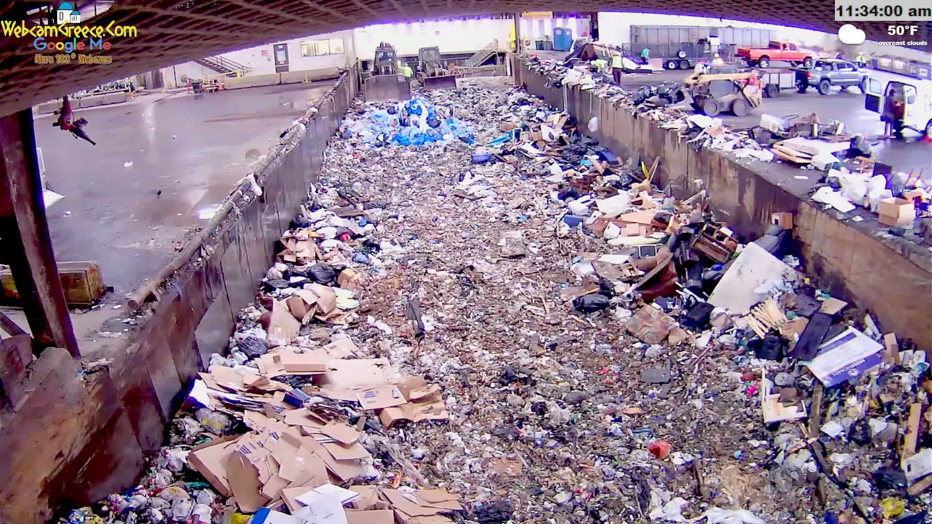 A large pile of trash and debris fills a long, open-topped container outdoors on an overcast day with a temperature of 50°F.