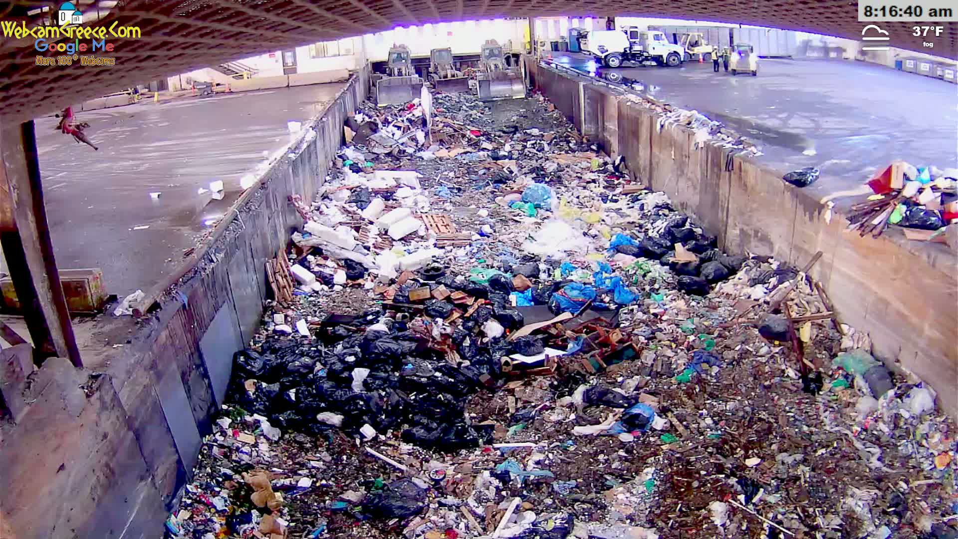 A large pile of garbage sits within a concrete trough in foggy, 37°F weather.