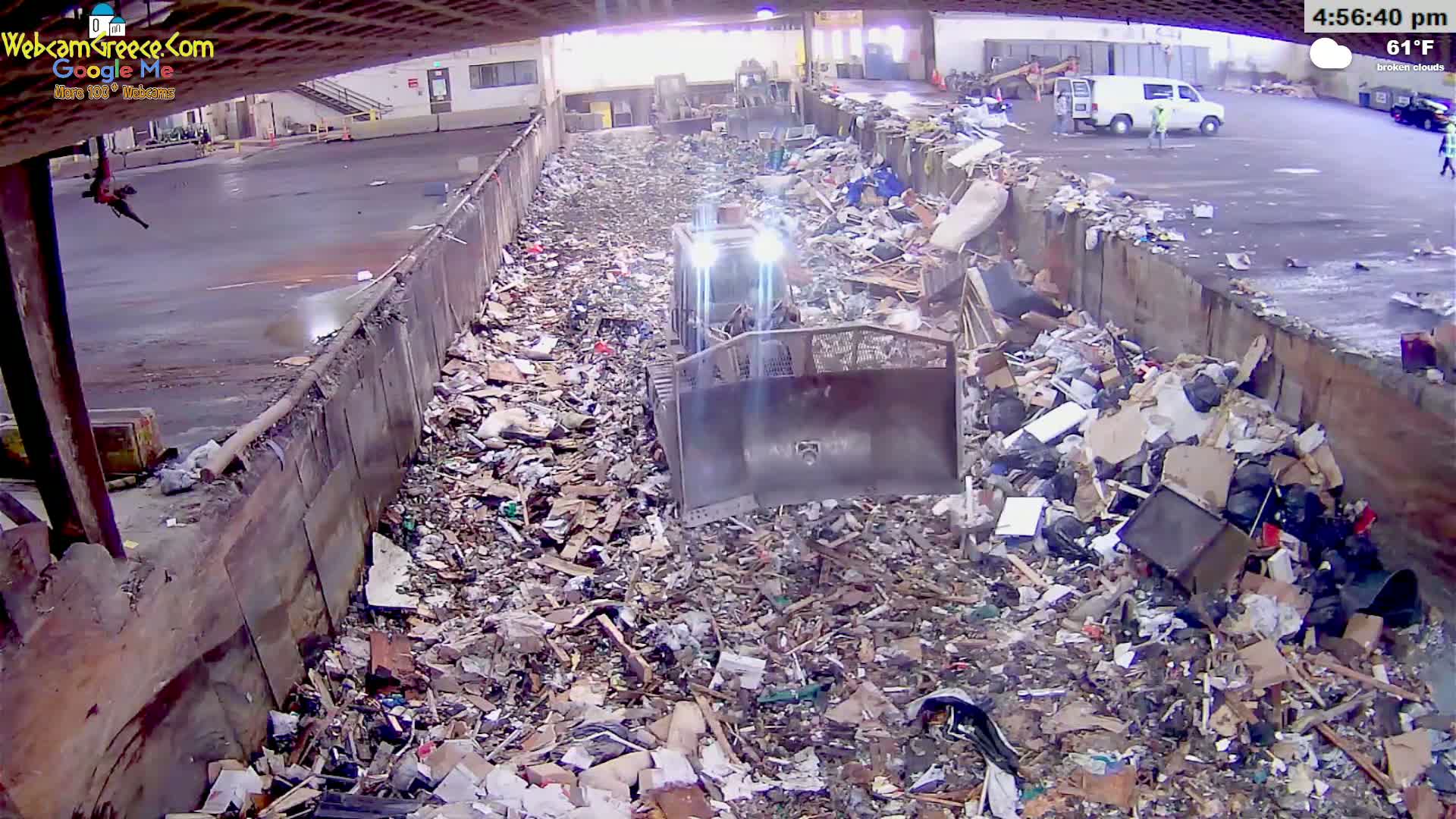 A bulldozer is working in a large pile of trash and debris within a high-walled enclosure on a partly cloudy day.