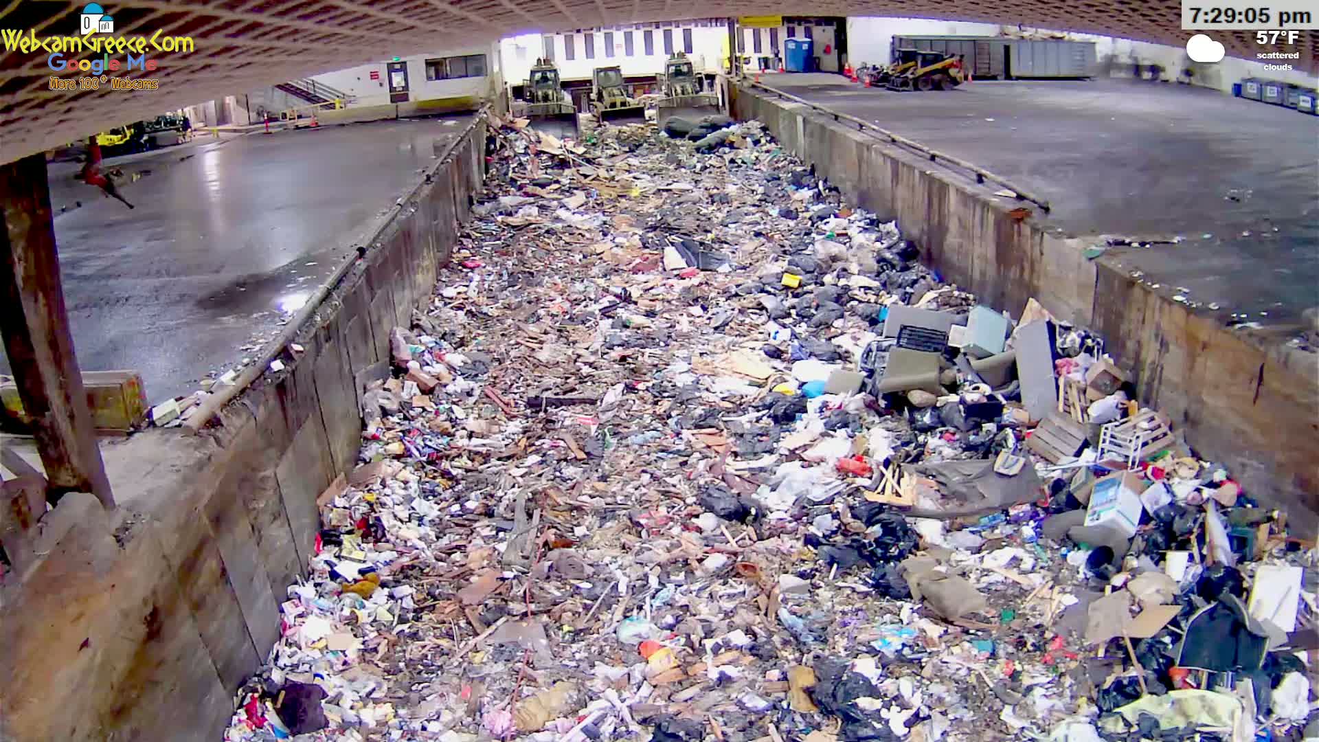 A large amount of trash and debris fills a concrete-walled disposal area under scattered clouds, in 57°F weather.