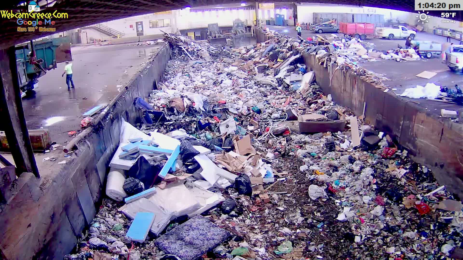 A large pile of trash sits in a waste disposal area under a clear sky.