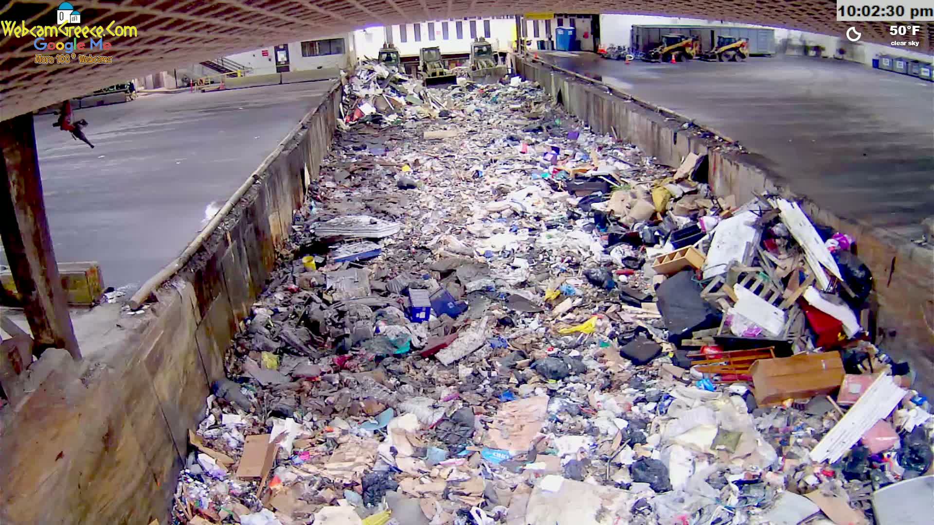 A large amount of trash and debris fills a long, narrow concrete trough under a clear sky at 50°F.