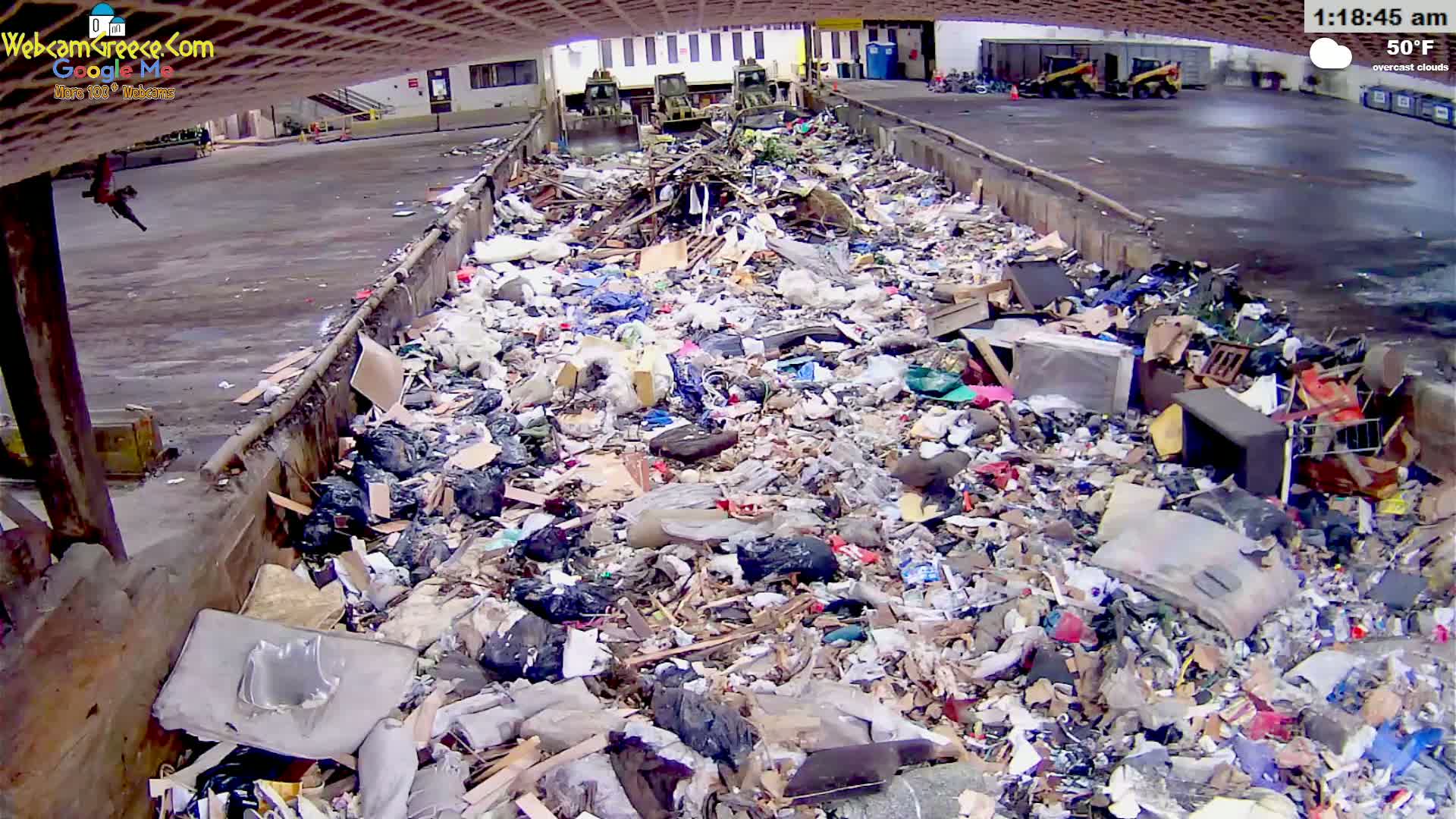 A large amount of trash and debris fills a long, narrow container outdoors under overcast skies on a 50°F day.