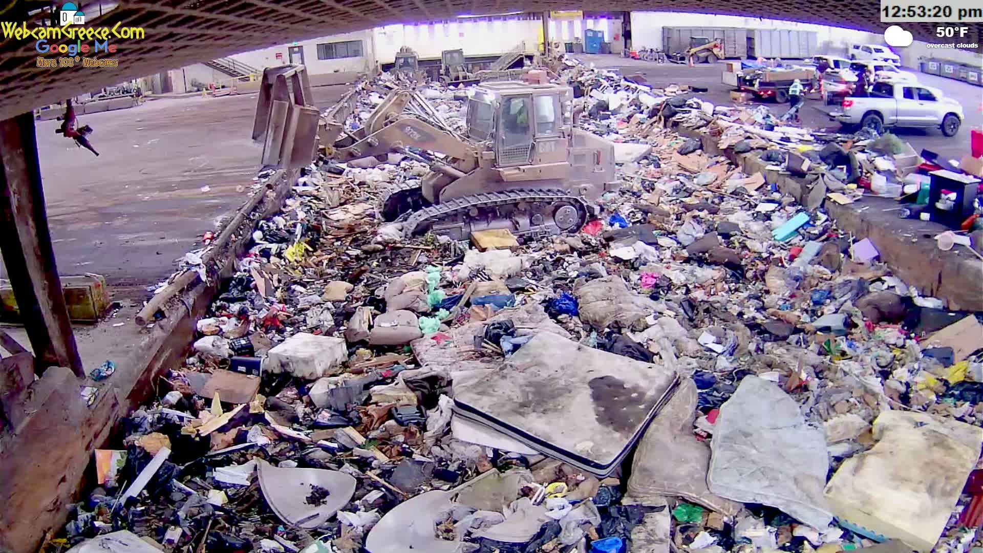 A bulldozer is working in an outdoor landfill filled with various types of trash under overcast skies.