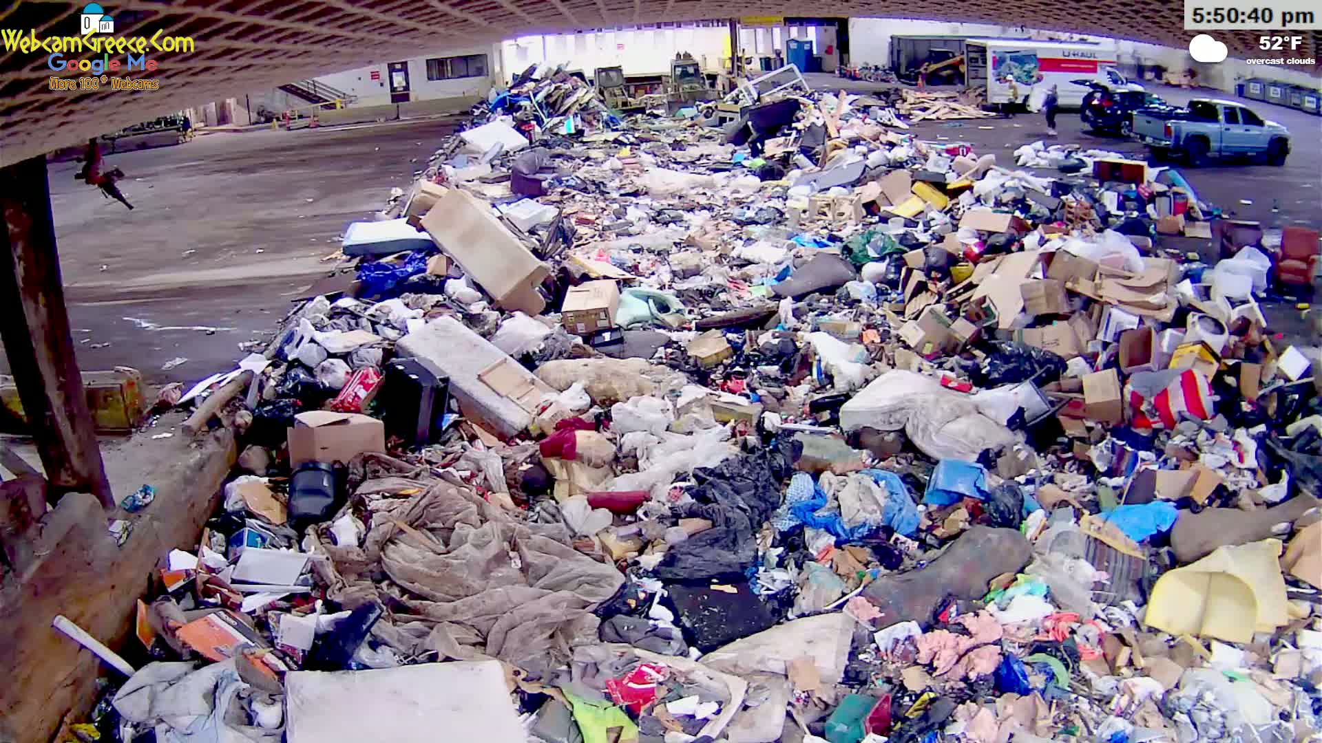 A large pile of discarded household items and debris sits in an outdoor area under overcast skies with a temperature of 52°F.