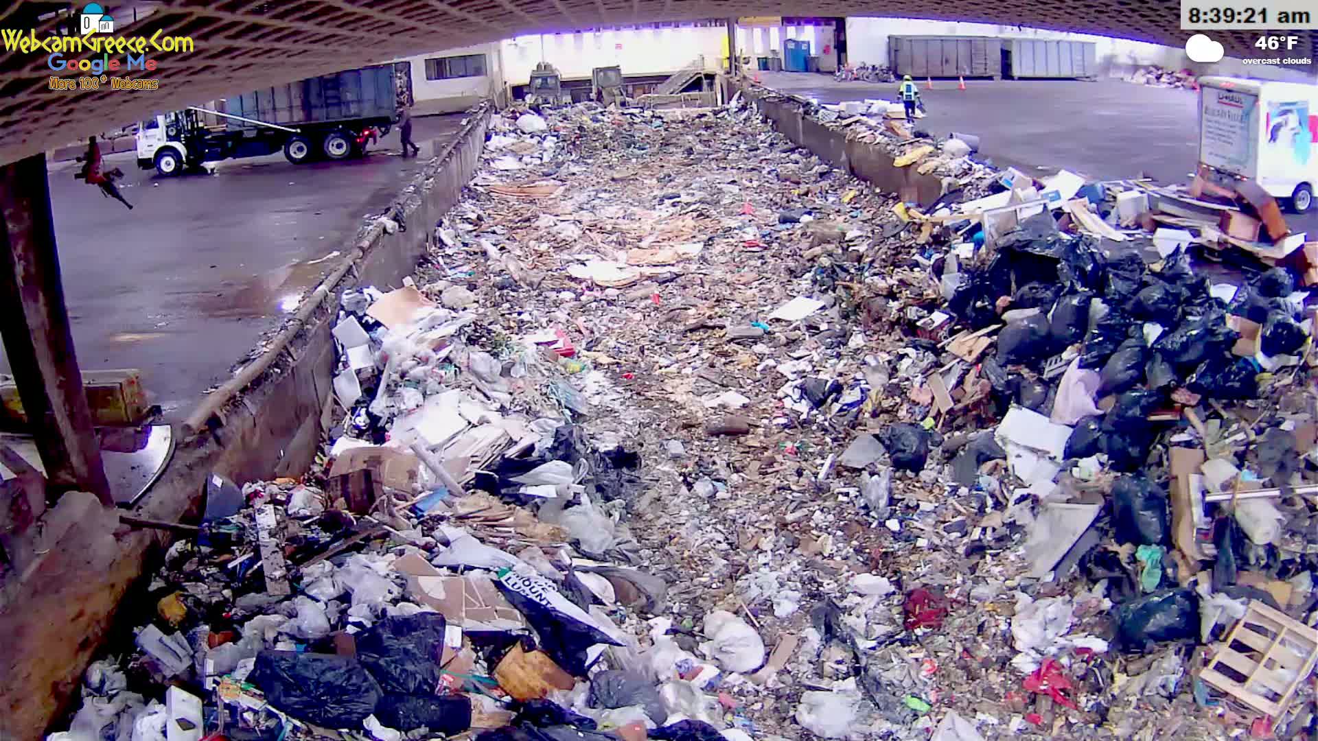 A large amount of trash and refuse is piled high in an outdoor waste receptacle under overcast skies.