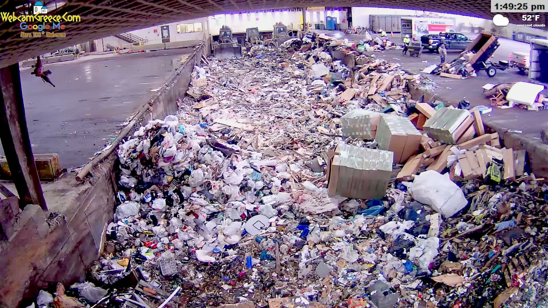 A large pile of mixed garbage and refuse is shown in an outdoor area under overcast skies, with a temperature of 52°F.