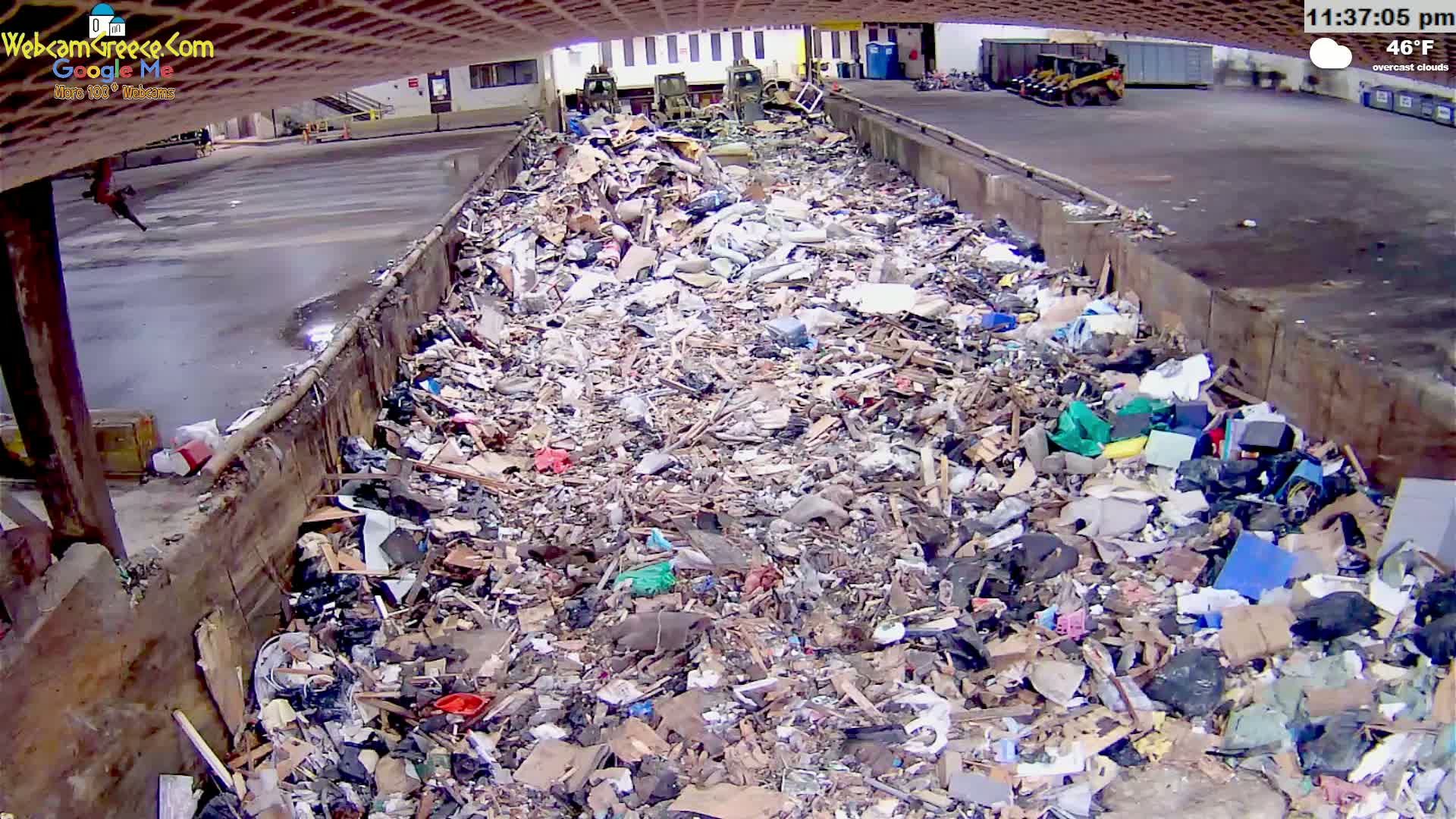 A large pile of mixed debris and trash fills a long, open container outdoors under overcast skies.