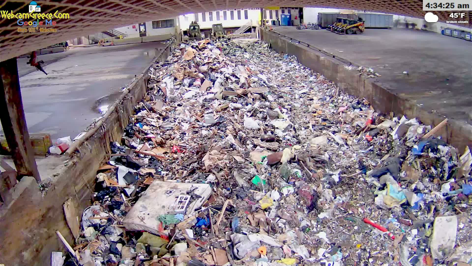 A large pile of trash fills a concrete trough under a partly cloudy sky at 45°F.