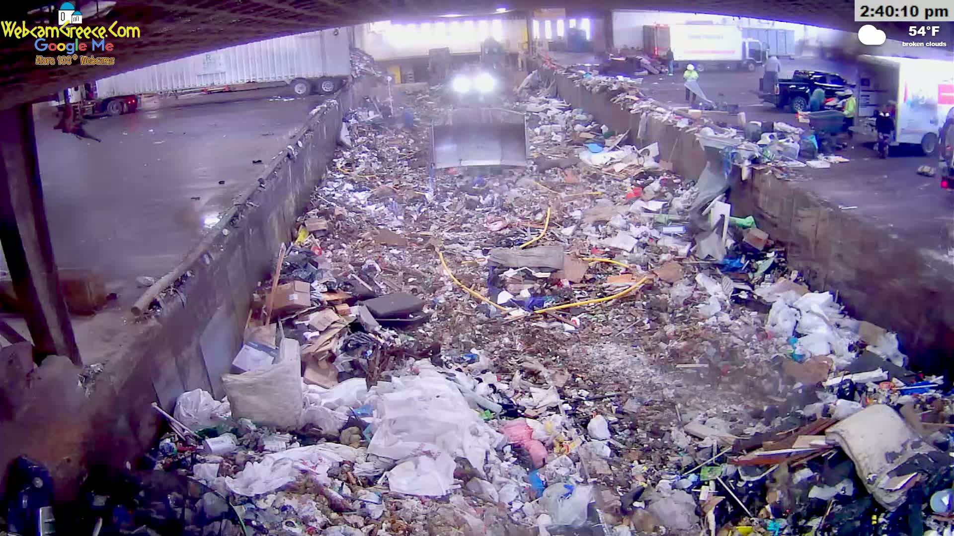A large amount of trash and debris fills a concrete pit outdoors under partly cloudy skies.