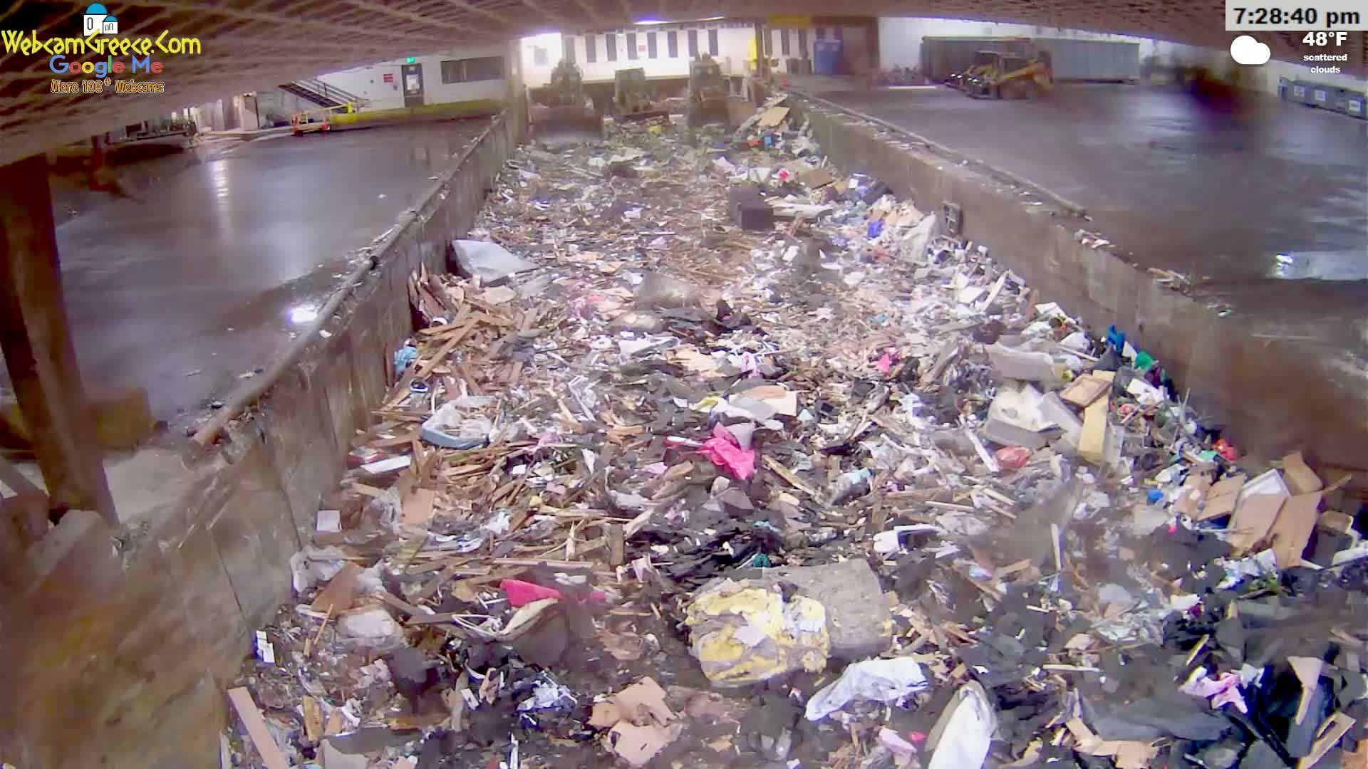 A large pile of trash and debris fills a concrete trough under an overcast sky.