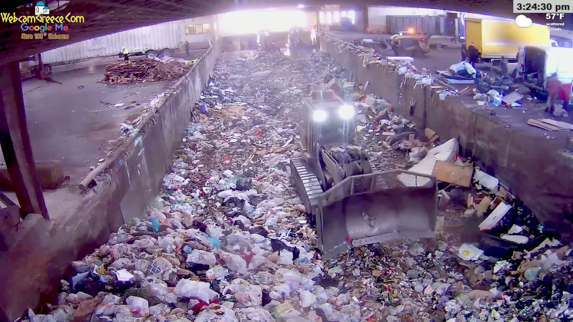 A bulldozer moves through a large pile of garbage under a partly cloudy sky.