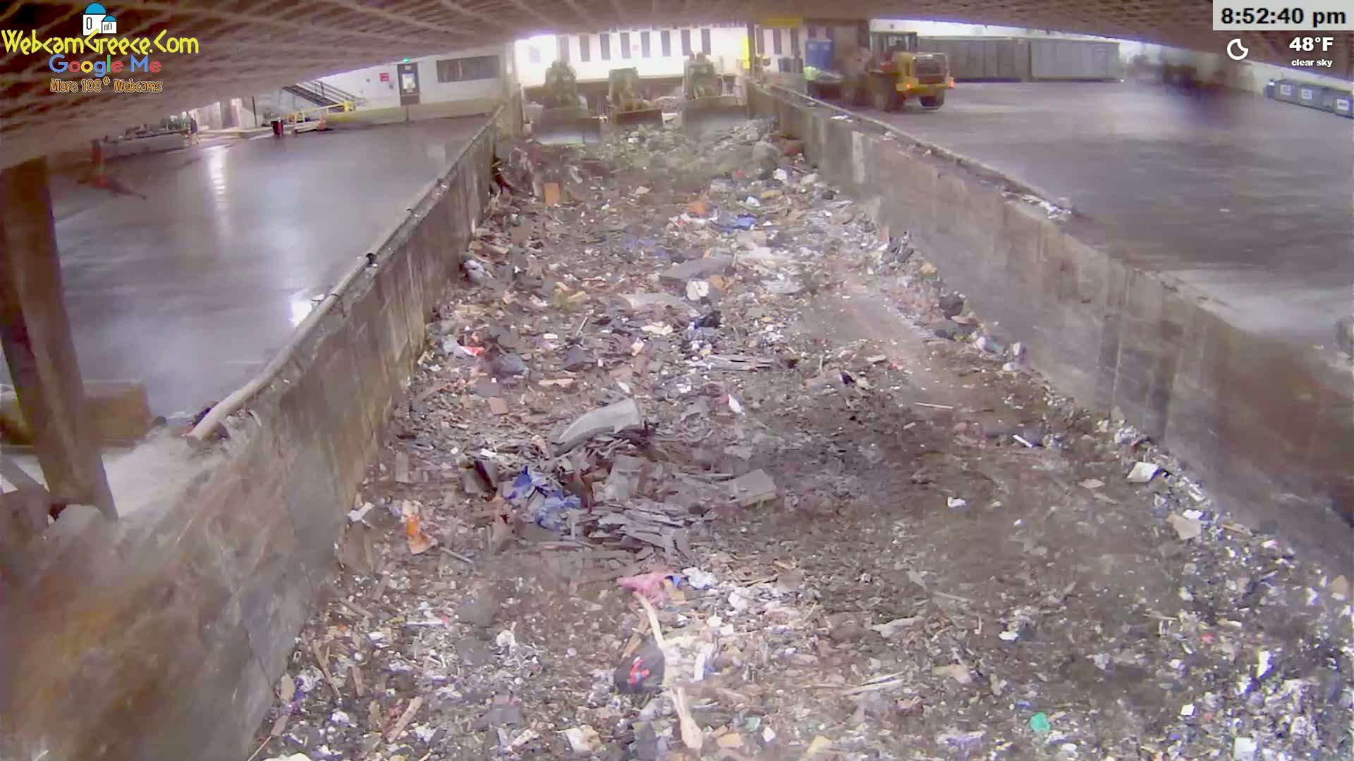 A large pile of debris and trash fills a long, narrow, concrete-walled area under a clear sky at 48°F.