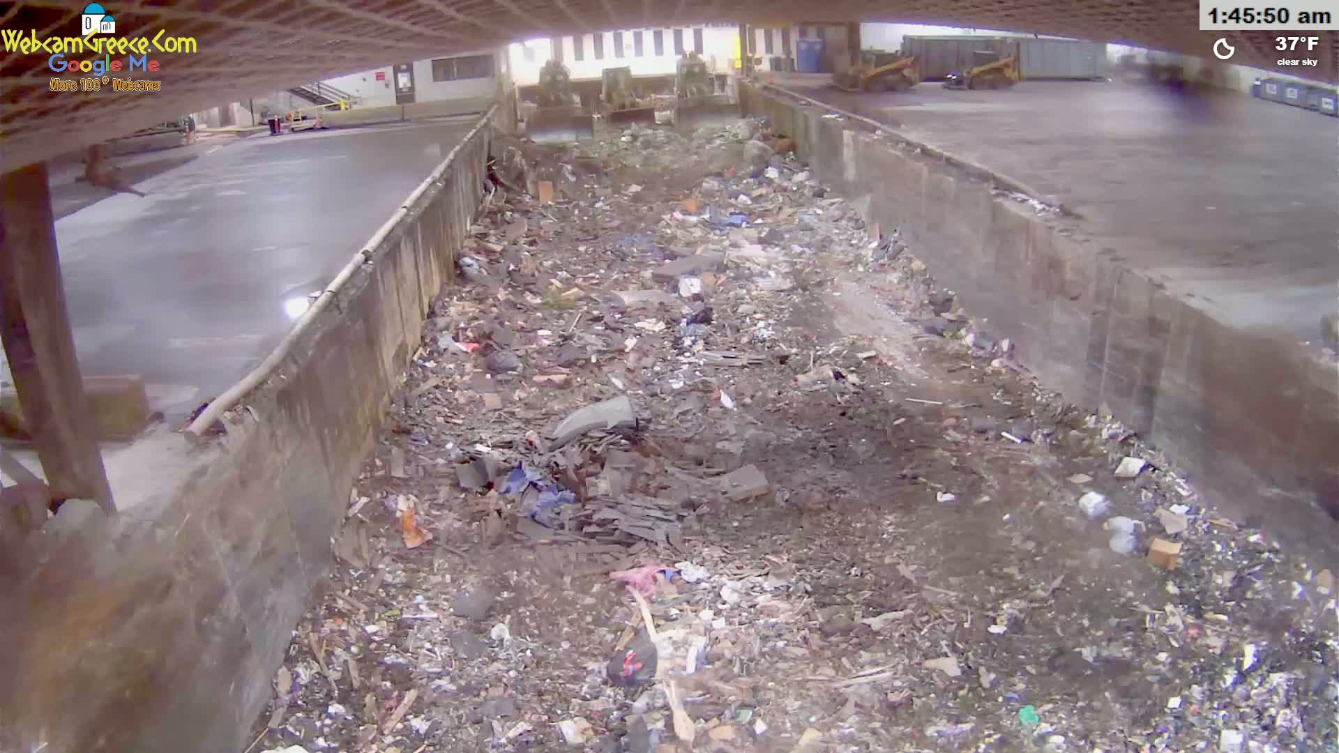 A large pile of trash and debris fills a long, narrow concrete trench under a clear sky at 37°F.