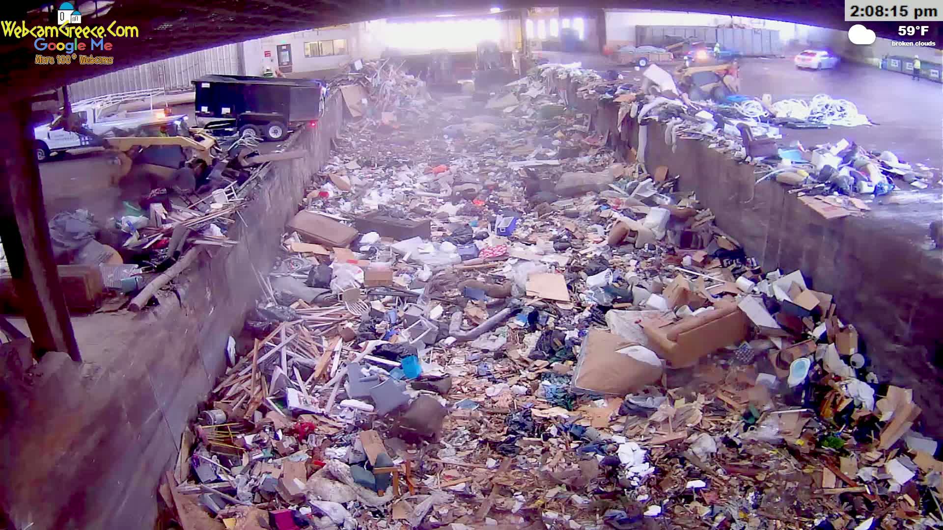 A large pile of refuse is seen in an outdoor, partially covered area under a broken cloudy sky, with a temperature of 59°F, and some construction equipment nearby.