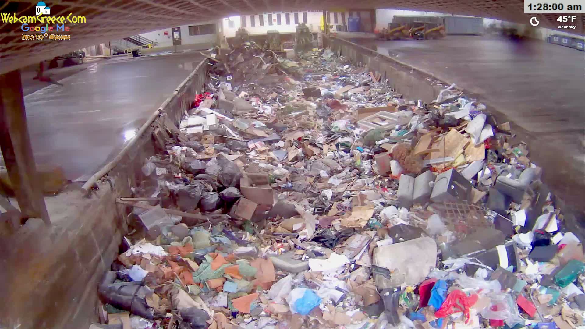 A large amount of trash and debris is piled high inside an industrial waste receptacle under a clear sky with a temperature of 45°F.