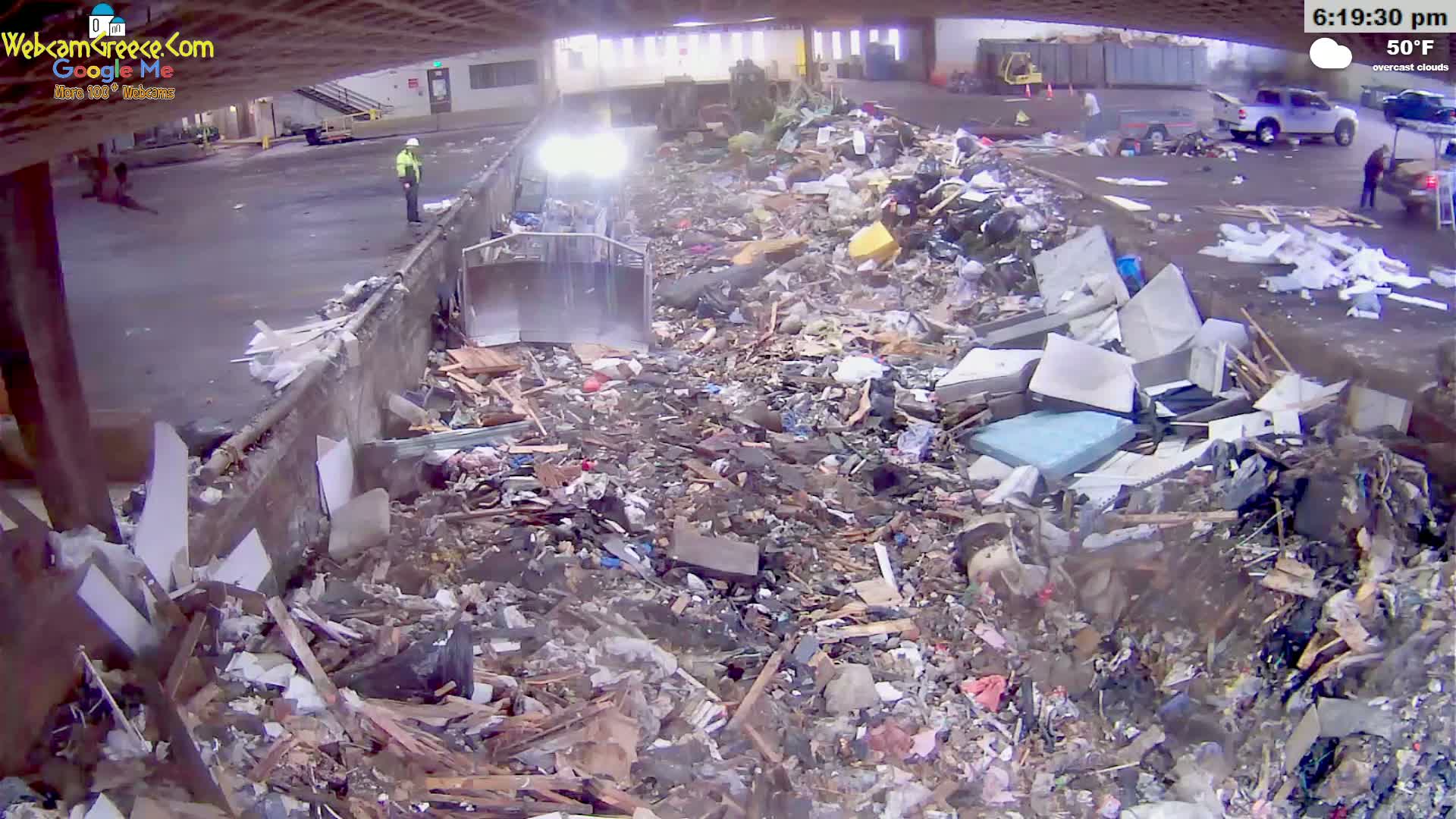 A large pile of debris and trash is being processed by a piece of heavy machinery under overcast skies.