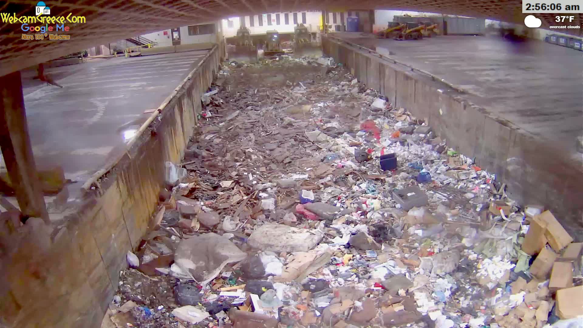 A large pile of trash and debris fills a concrete-walled trough under overcast skies at 37°F.