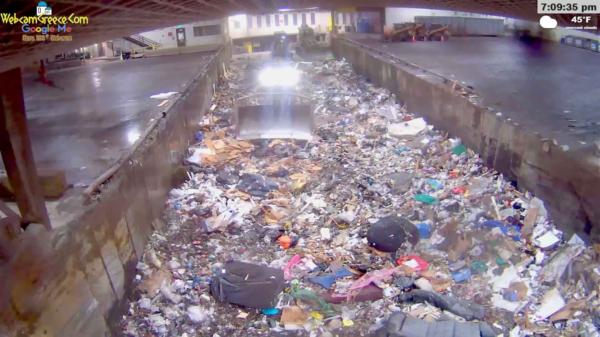 A large pile of garbage fills a concrete trough under overcast skies at 45°F.