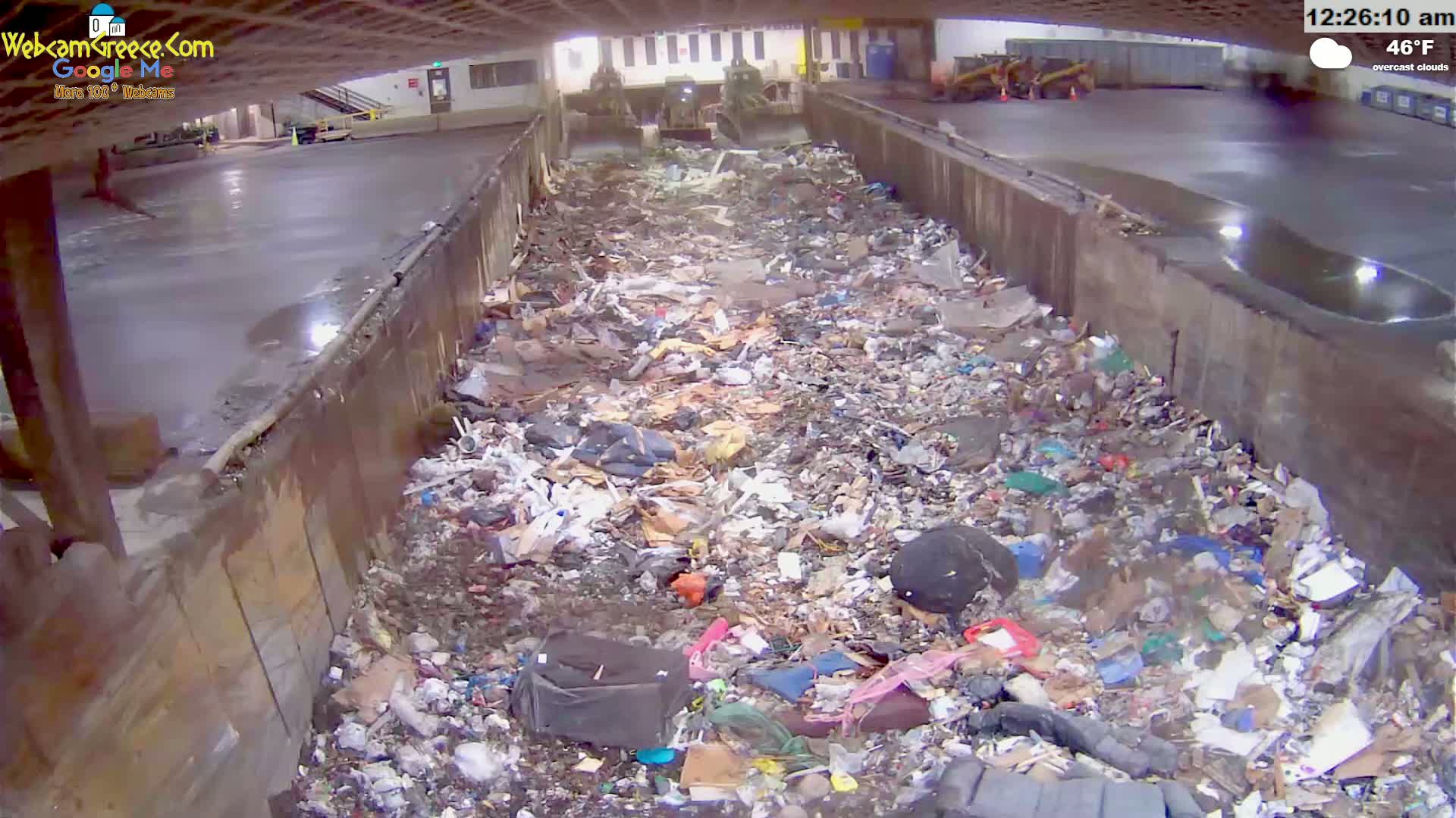 A large pile of trash sits in a concrete trough under overcast skies.