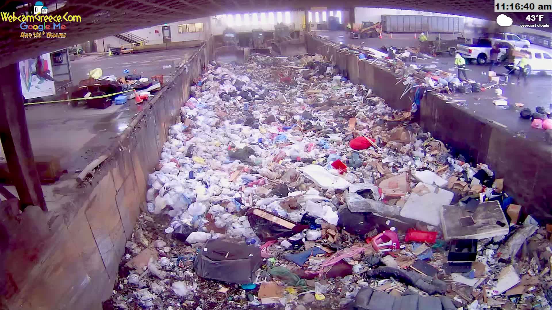 A large pile of trash fills a concrete trough outdoors under overcast skies.