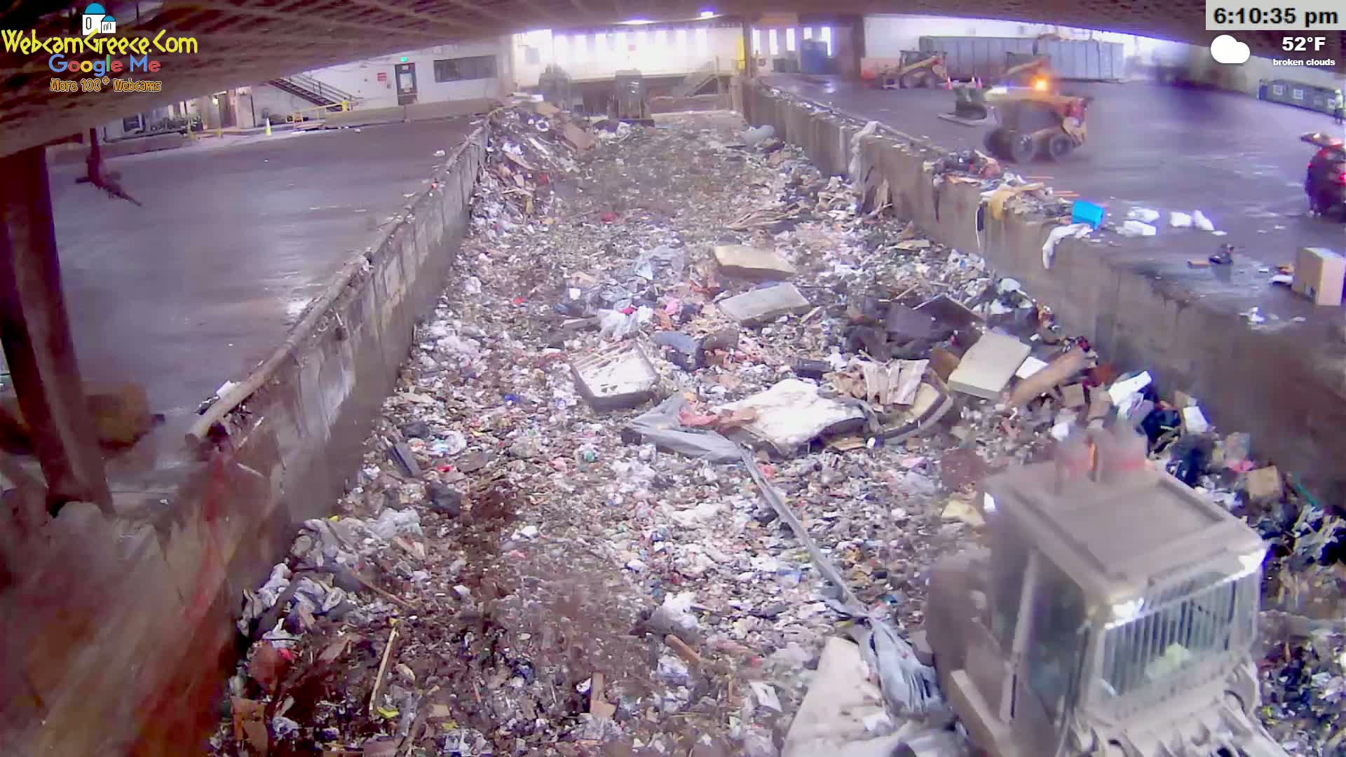 A large pile of trash is seen in a waste disposal area under a partly cloudy sky, with machinery nearby.