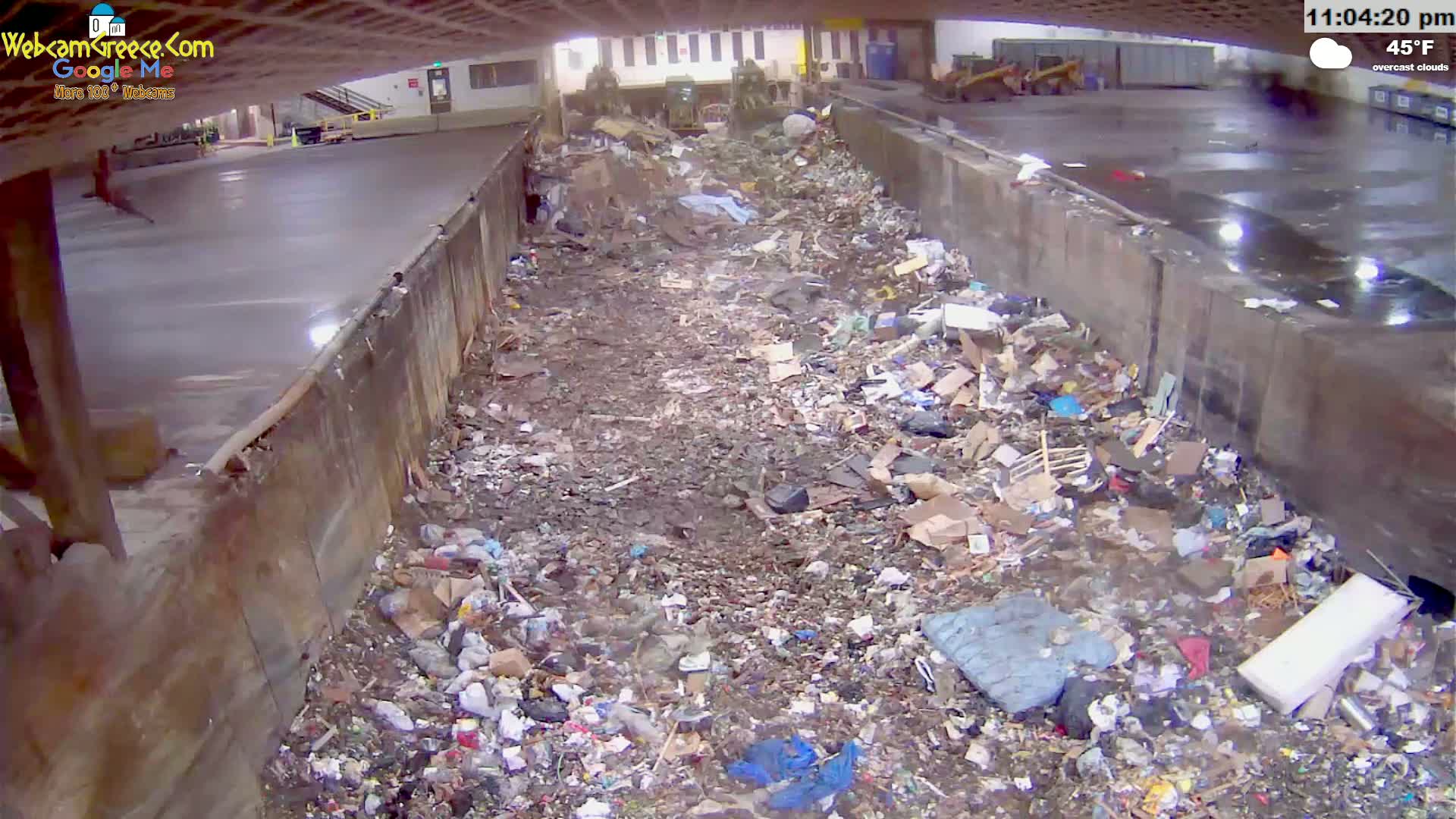 A large pile of trash and debris fills a concrete trough under overcast skies, with the temperature at 45°F.