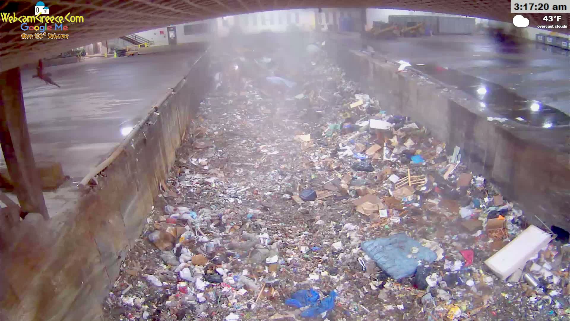 A large pile of trash and debris fills a concrete-walled area outdoors under overcast skies.