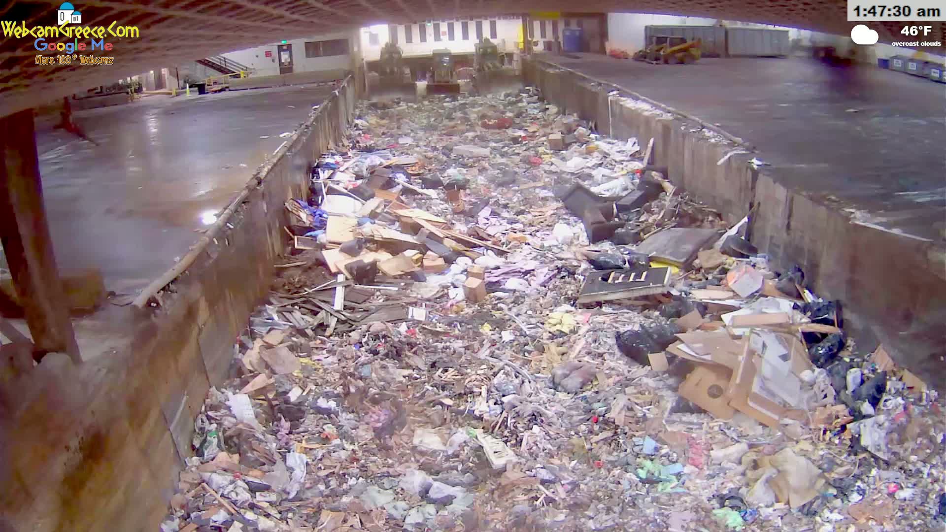 A large pile of trash and debris fills a concrete waste receptacle under overcast skies.