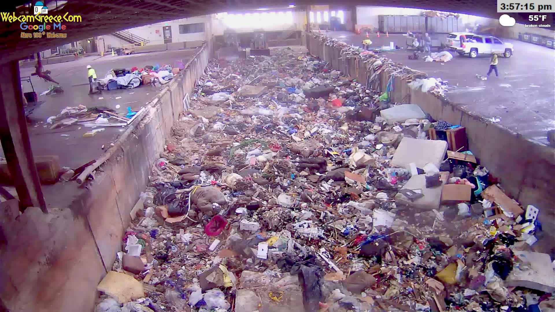 A large pile of trash is contained within concrete walls under a partly cloudy sky with a temperature of 55°F.