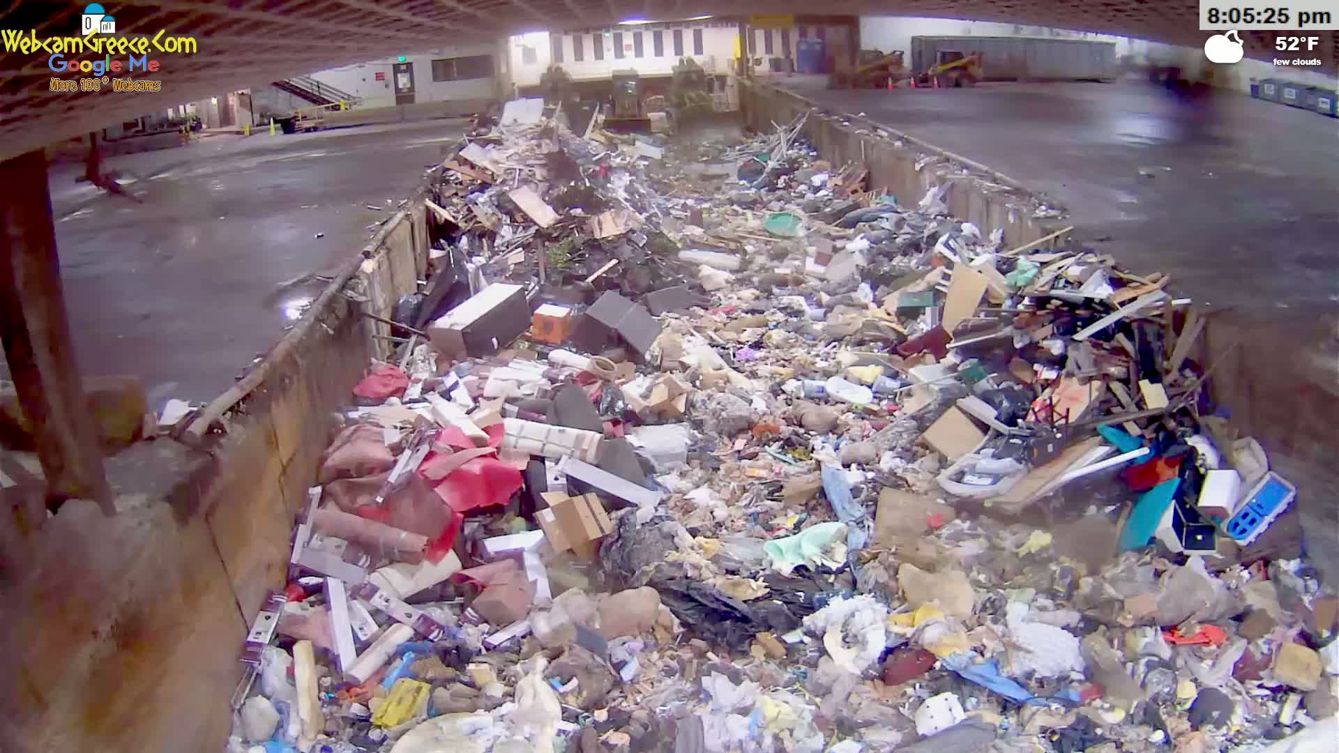 A large metal container is overflowing with a diverse pile of trash under a partly cloudy sky.