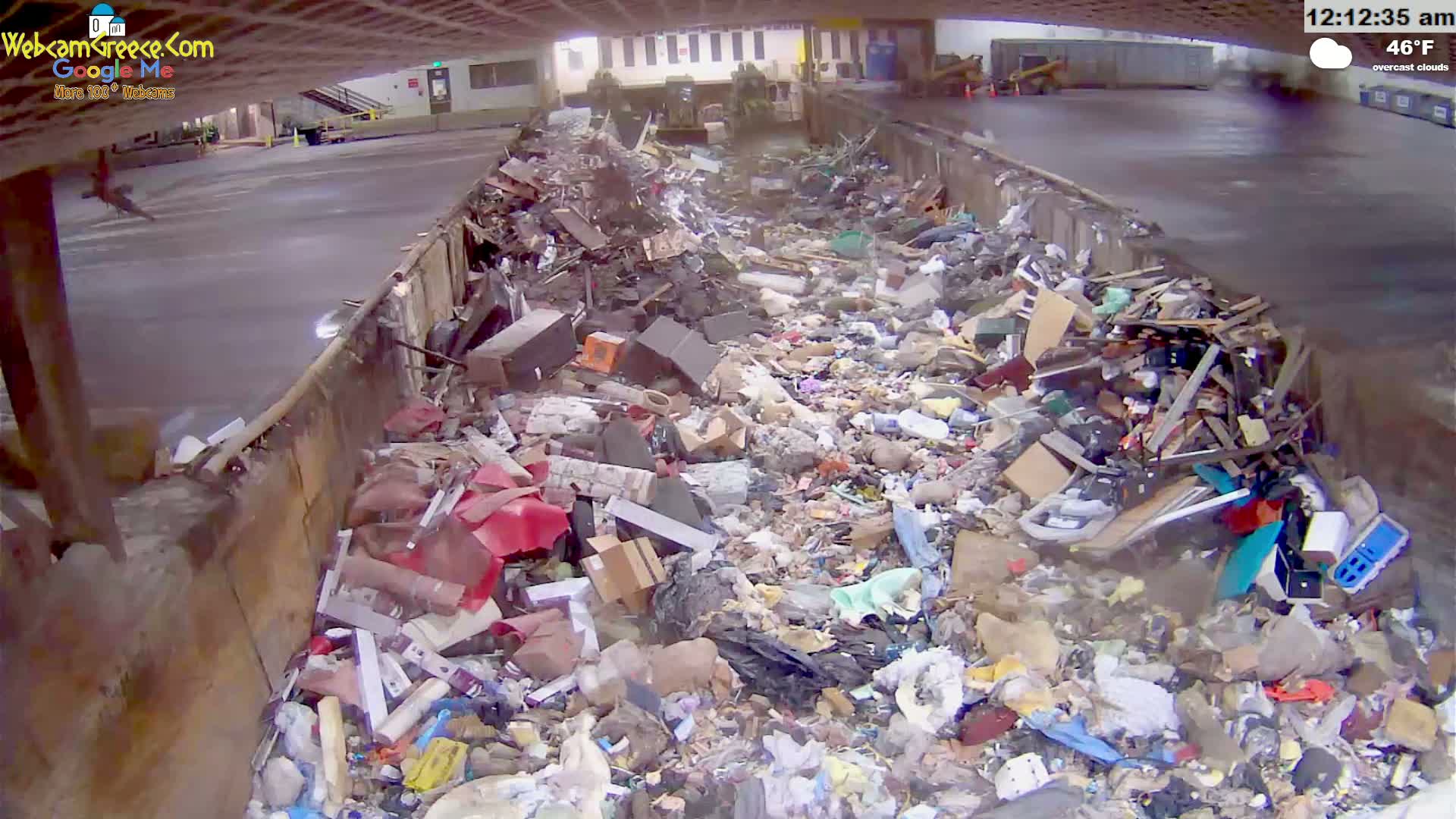 A large dumpster is overflowing with a variety of trash under overcast skies.