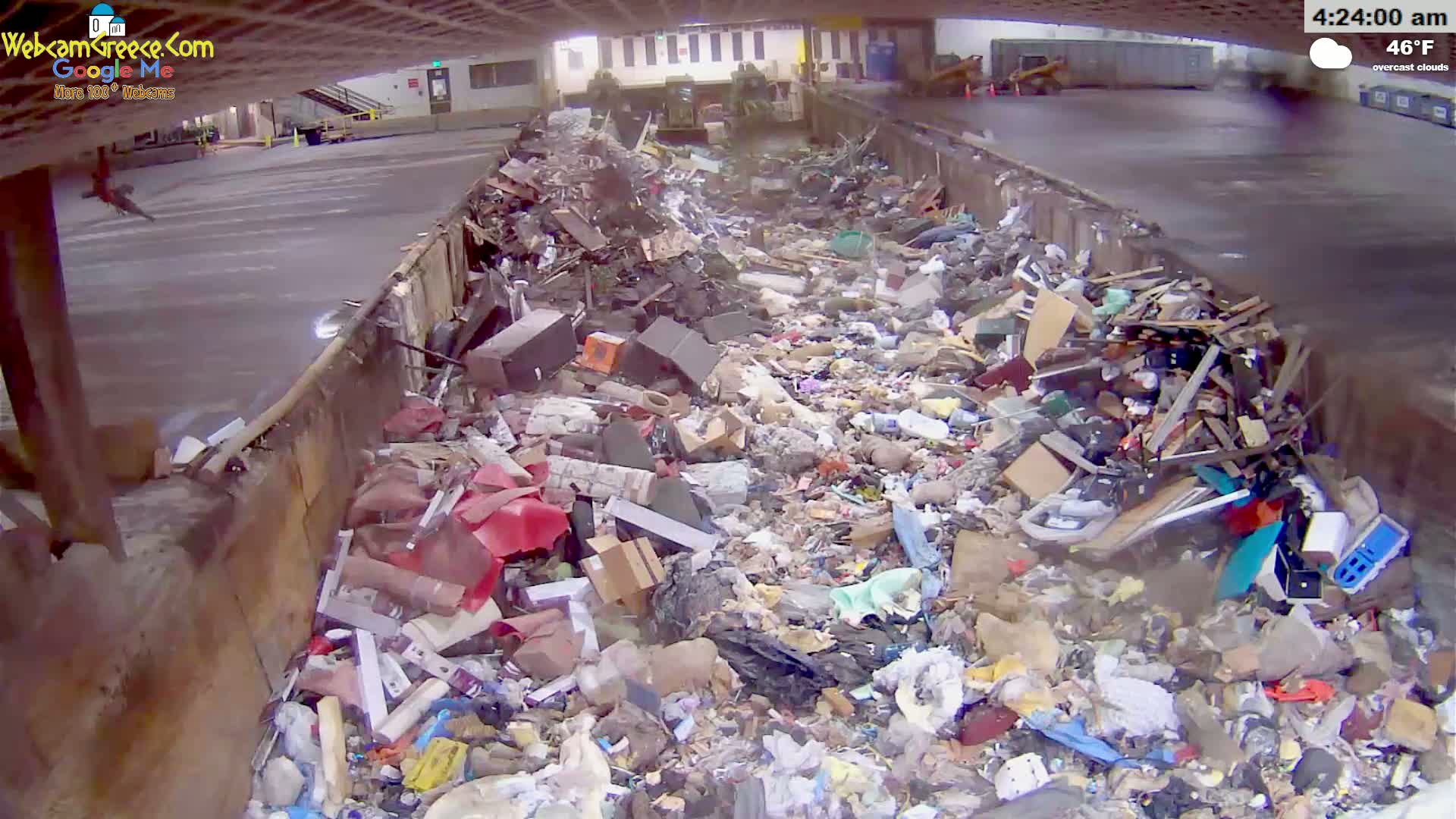A large container is overflowing with a variety of trash and debris under overcast skies.