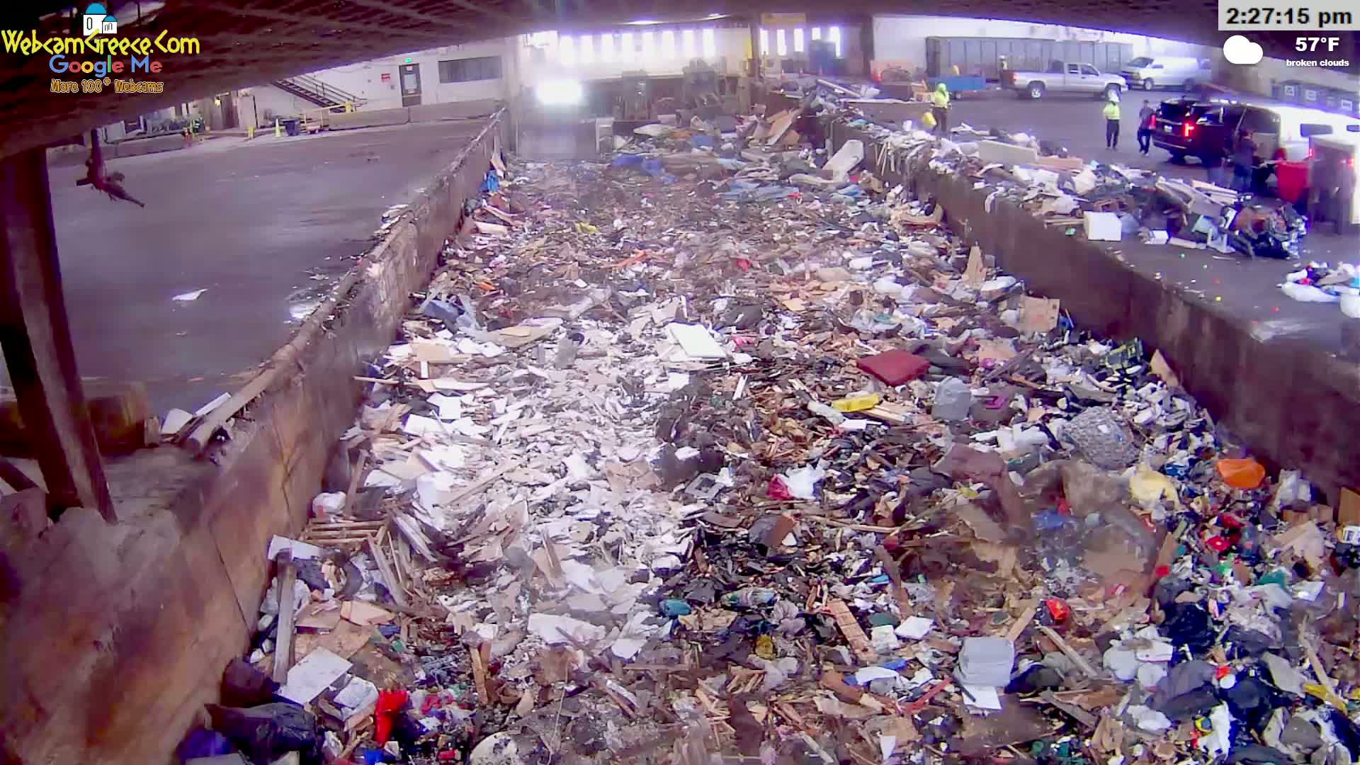 A large pile of refuse is seen under a partly covered outdoor area with broken clouds and a temperature of 57°F.