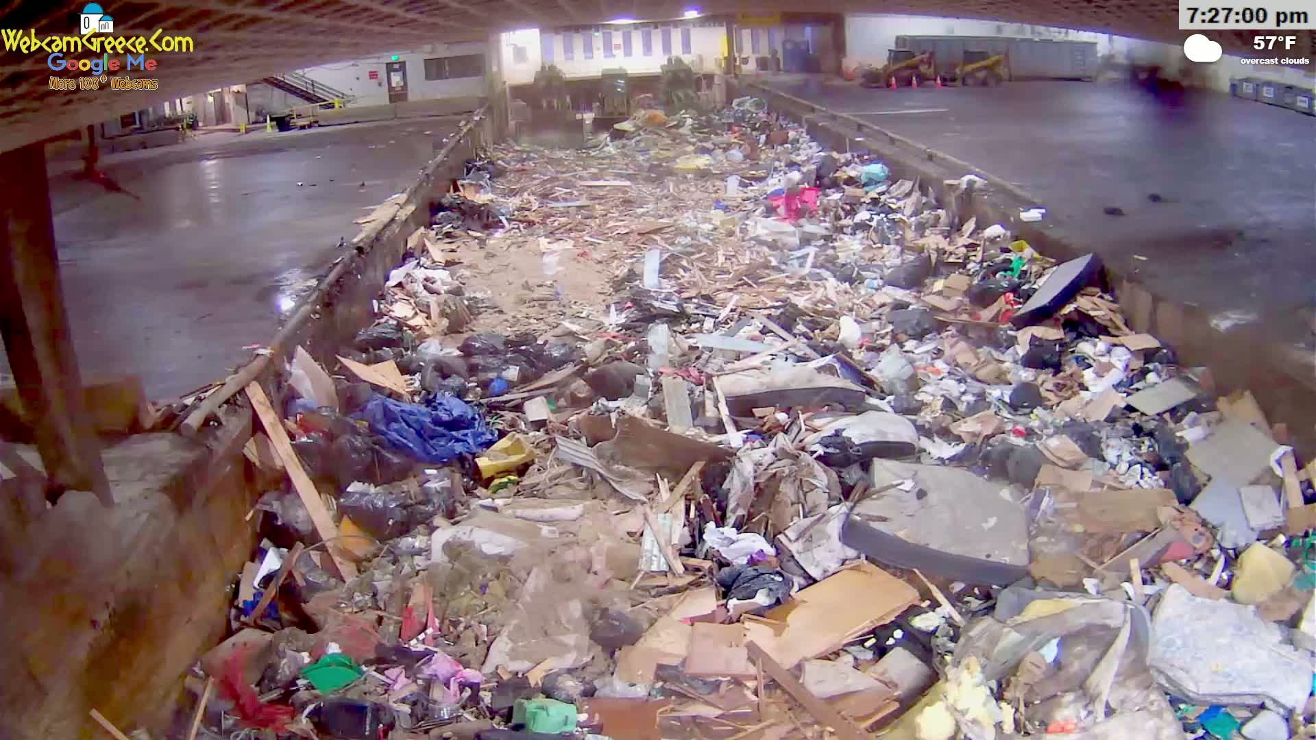 A large pile of garbage and debris fills a concrete-lined area under overcast skies at 57°F.