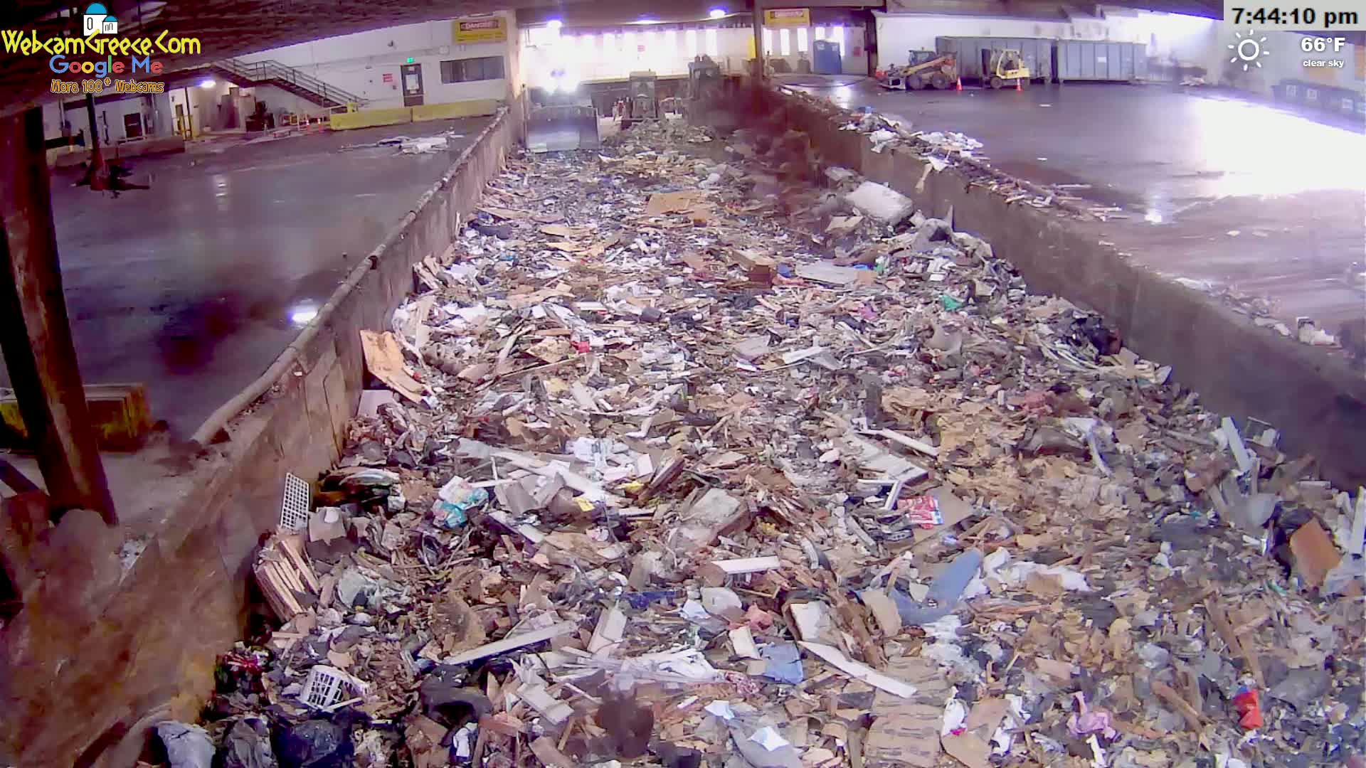A large amount of refuse is piled high inside a long, concrete trough under a clear sky.