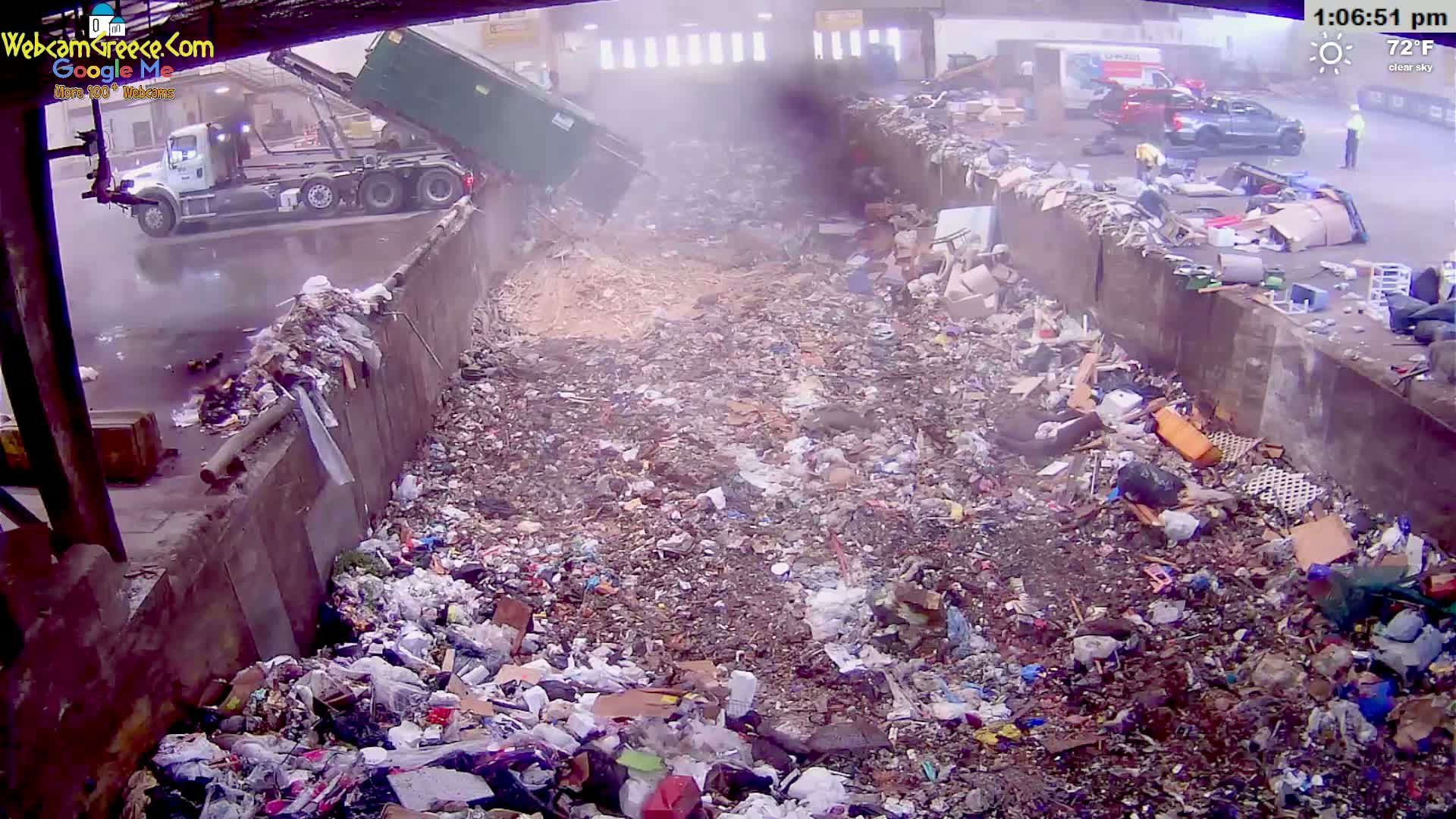 A garbage truck dumps its load of trash into a large landfill on a clear 72°F day.