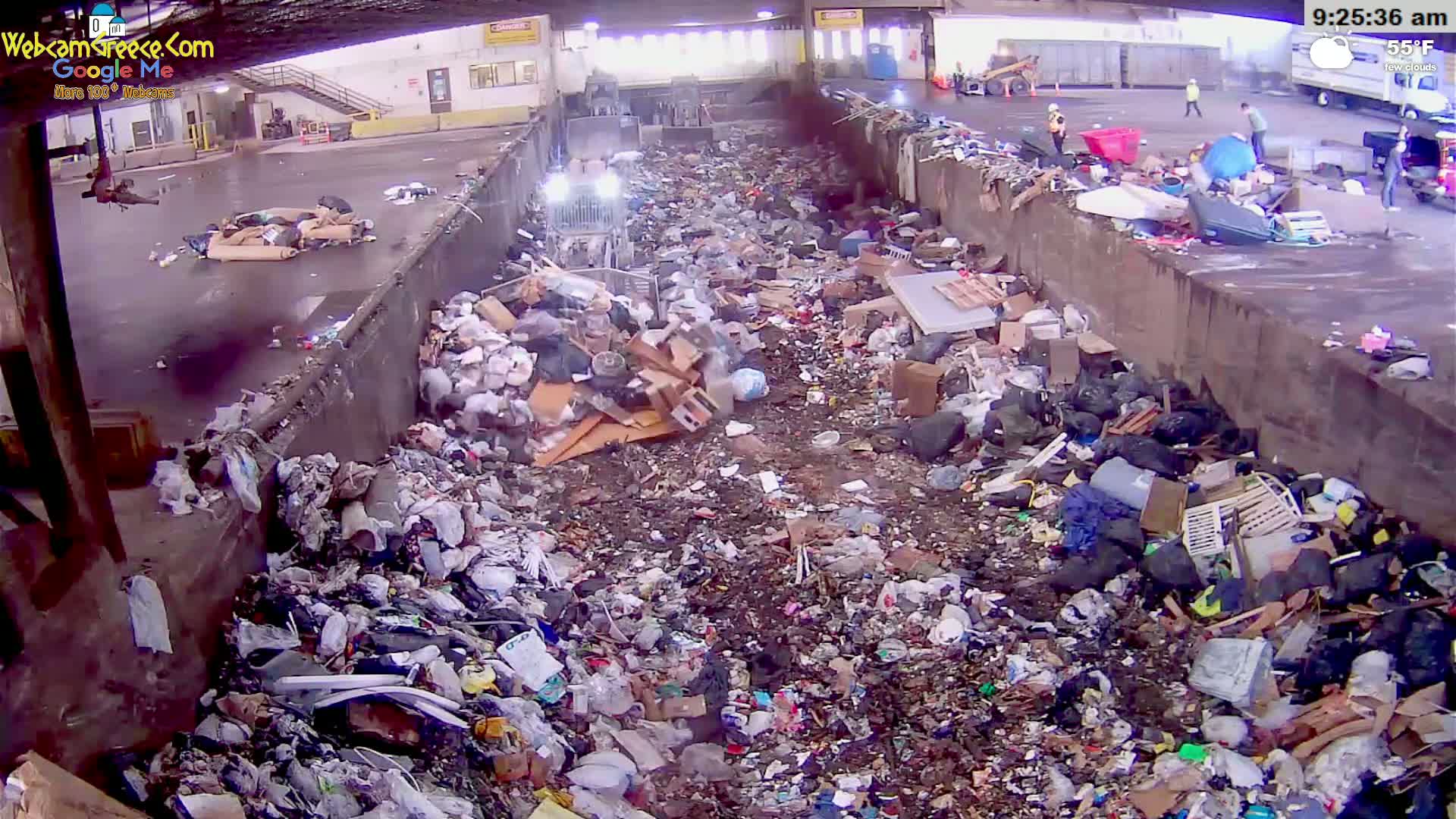 A large amount of trash and debris is piled up in a concrete-walled area outdoors on a slightly cool, partly cloudy morning.